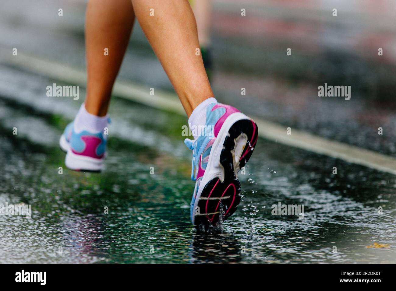 Nahaufnahme Teilbeine Läuferin in Laufschuhen läuft auf nassem Asphalt, Tropfen und Spritzwasser Stockfoto