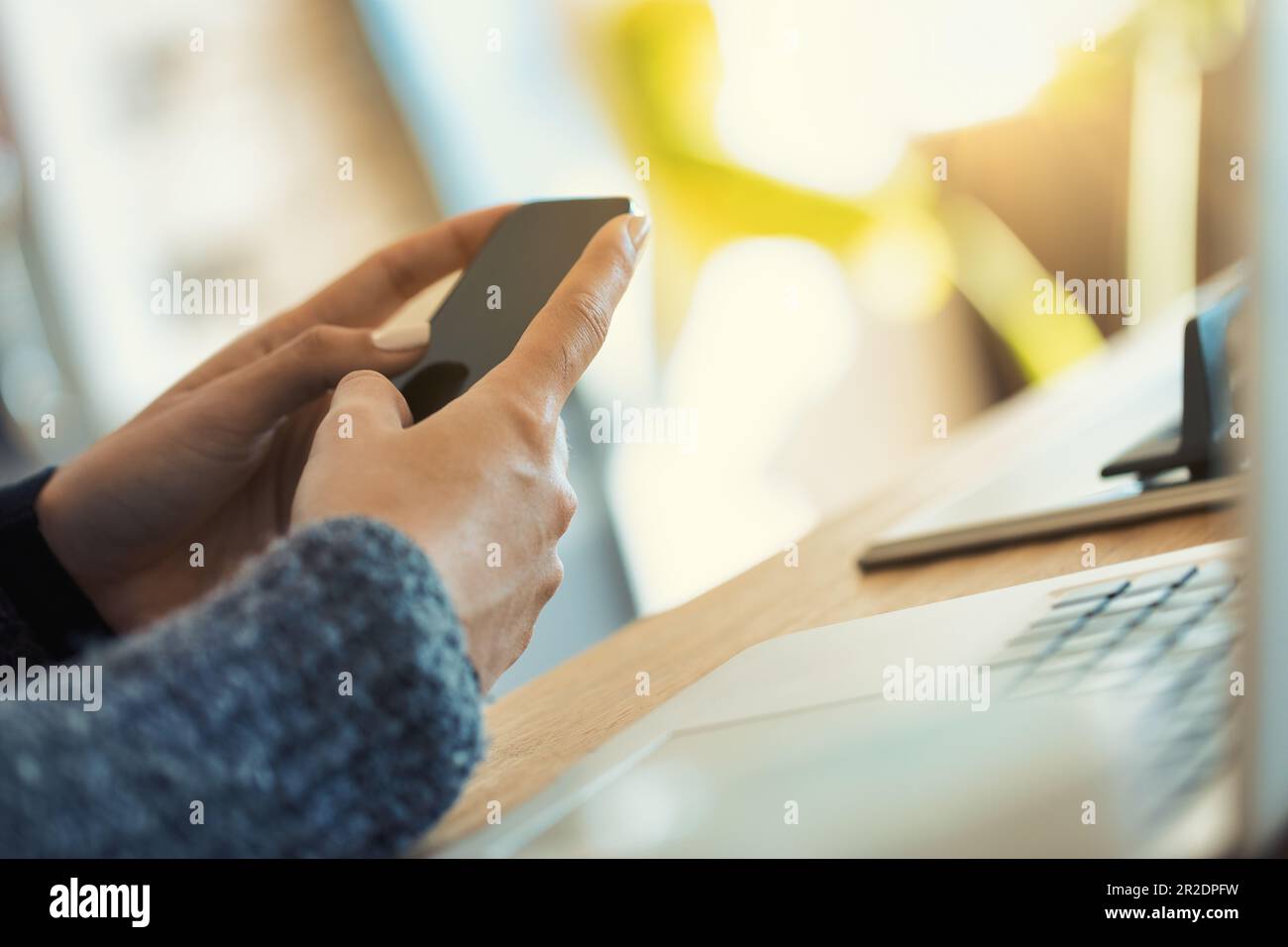 In einer modernen Küche bedienen gut gepflegte Hände einer gesichtslosen Frau ein Smartphone und einen Laptop und arbeiten möglicherweise mit Kaffeebedarf Stockfoto