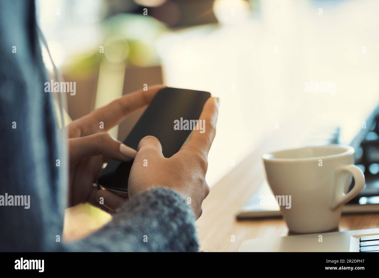 In einer modernen Küche bedienen gut gepflegte Hände einer gesichtslosen Frau ein Smartphone und einen Laptop und arbeiten möglicherweise mit Kaffeebedarf Stockfoto
