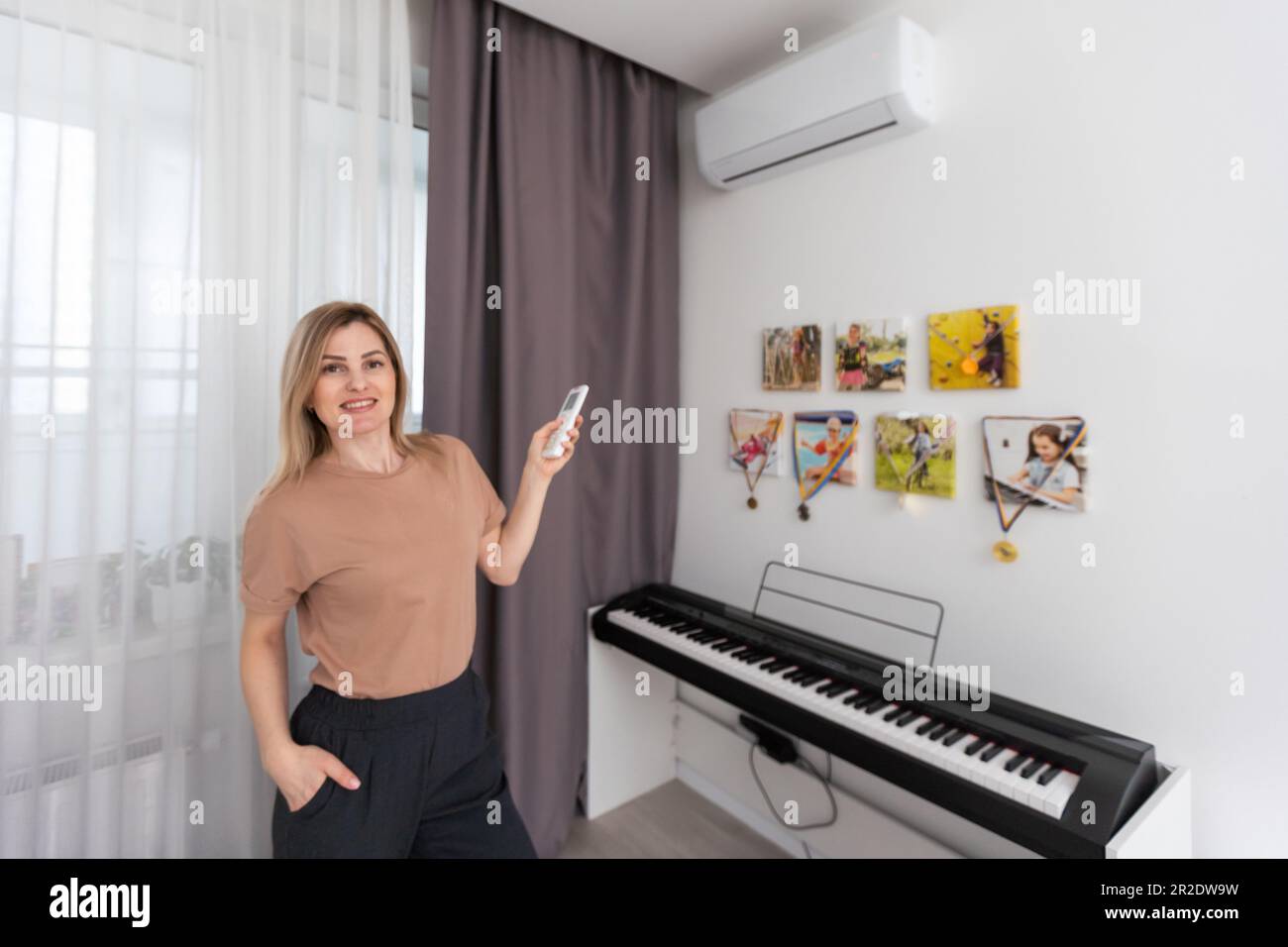 Frau mit Fernbedienung, die auf die Klimaanlage gerichtet ist Stockfoto