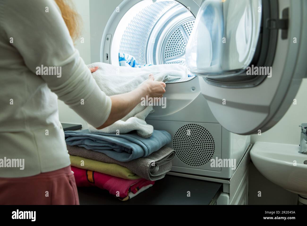 Eine Frau, die Wäsche macht. Trockner in einem Landry-Raum zu Hause zum Trocknen von Kleidung. Hausfrau entlädt Trockner und faltbare saubere und trockene Bettwäsche. Hausarbeit Stockfoto