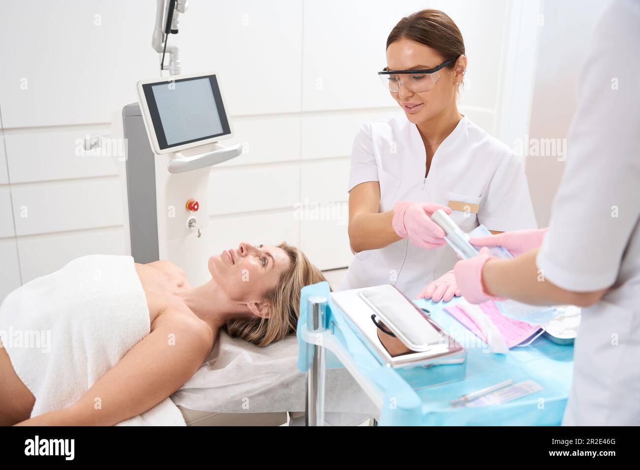 Assistentin geht Kosmetikerin in Schutzbrille für kosmetische Eingriffe Stockfoto