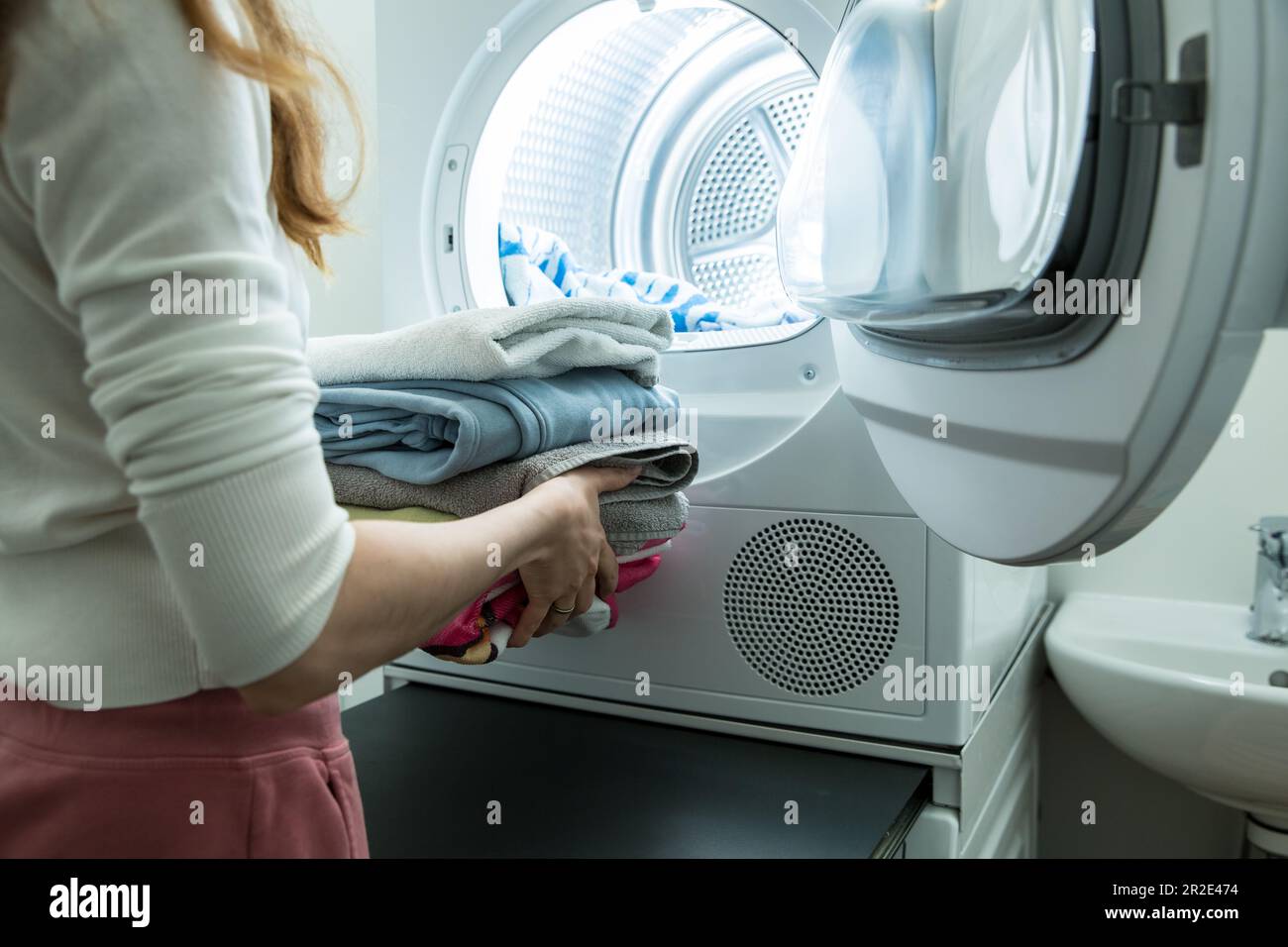 Eine Frau, die Wäsche macht. Trockner in einem Landry-Raum zu Hause zum Trocknen von Kleidung. Hausfrau entlädt Trockner und faltbare saubere und trockene Bettwäsche. Hausarbeit Stockfoto