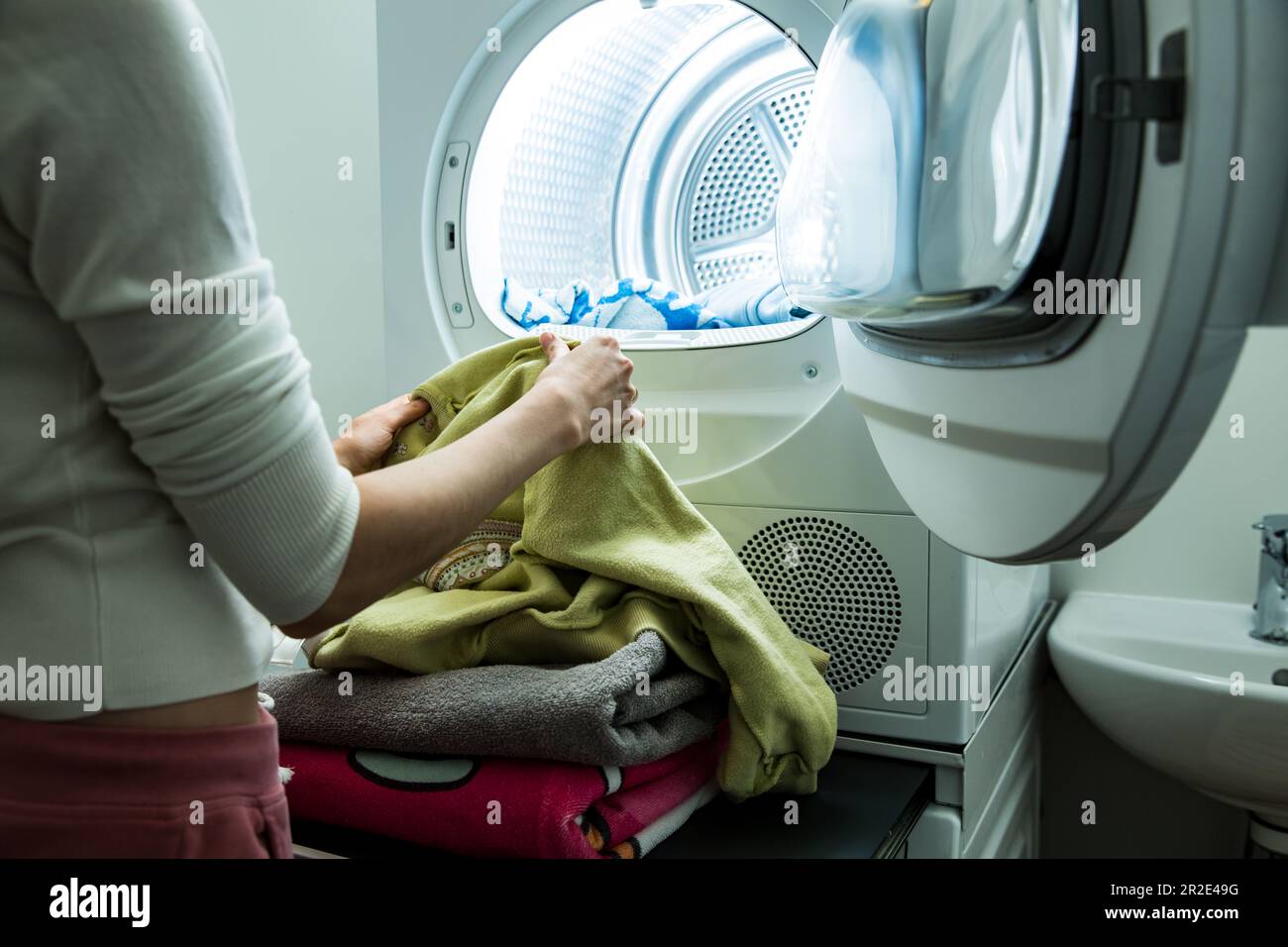 Eine Frau, die Wäsche macht. Trockner in einem Landry-Raum zu Hause zum Trocknen von Kleidung. Hausfrau entlädt Trockner und faltbare saubere und trockene Bettwäsche. Hausarbeit Stockfoto