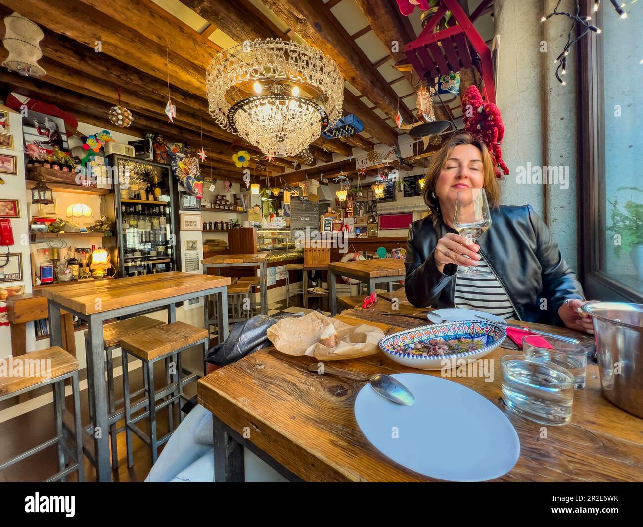Glückliche weiße Frau, die ein Glas Weißwein im Restaurant trinkt. Eine attraktive Frau, die Wein beim Dating genießt. Winter in Venedig, Italien Konzept Stockfoto