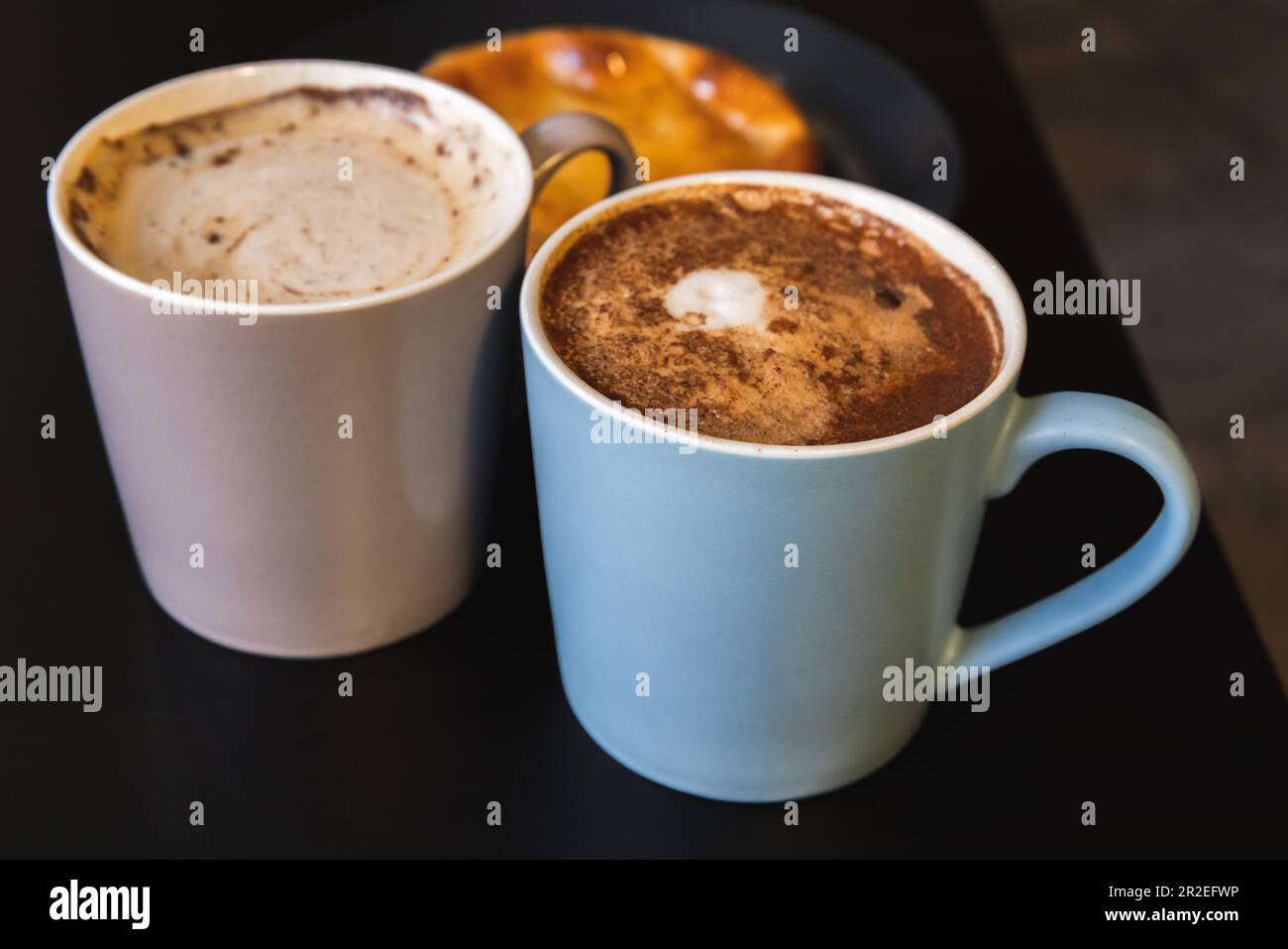 Zwei Cappuccino. Tassen voller Kaffee mit Milchschaum und Zimtpulver stehen auf einem schwarzen Tisch, Nahaufnahme mit selektivem Weichzeichner Stockfoto Zwei Cappuccino. Tassen voller Kaffee mit Milchschaum und Zimtpulver stehen auf einem schwarzen Tisch, Nahaufnahme mit selektivem Weichzeichner Stockfoto