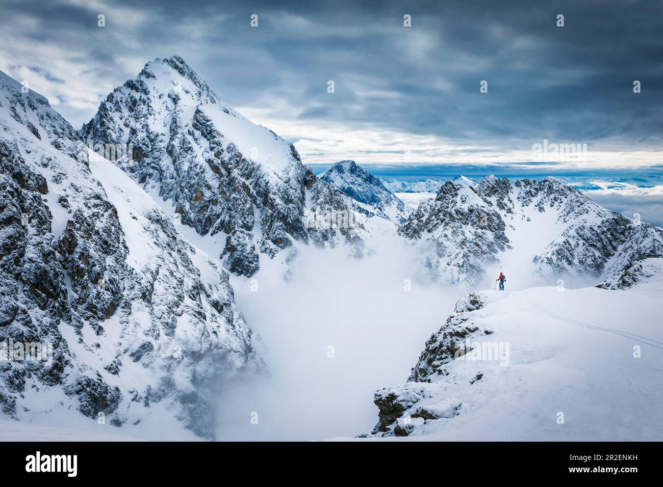 Skifahrer stehen auf einem Felsvorsprung in der Mieminger Kette vor einer majestätischen Bergkulisse mit mystischer Wolkenatmosphäre in Tirol, Österreich Stockfoto