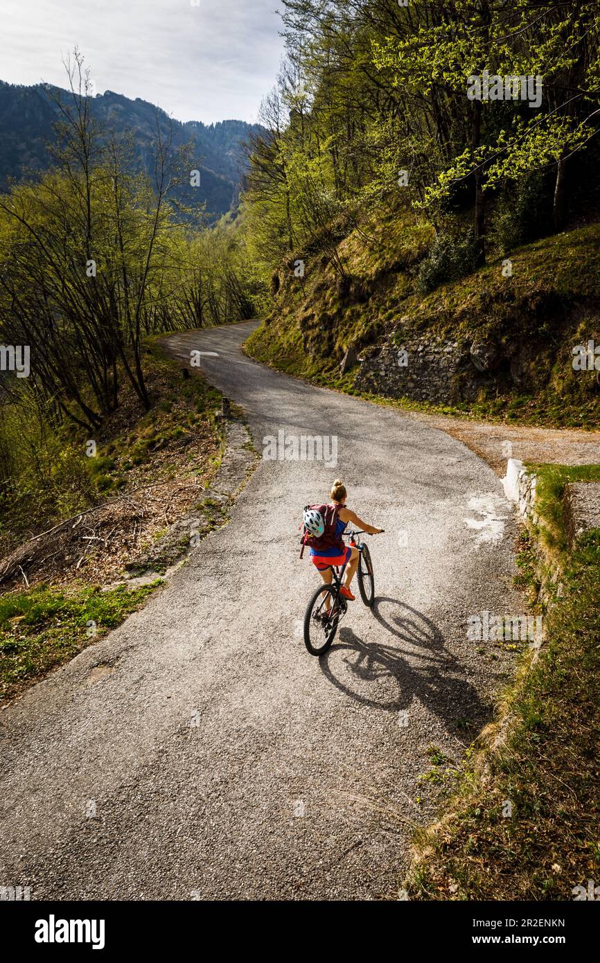 Junge Frau fährt mit dem Mountainbike eine enge Asphaltstraße hinauf, Idro-See, Italien Stockfoto