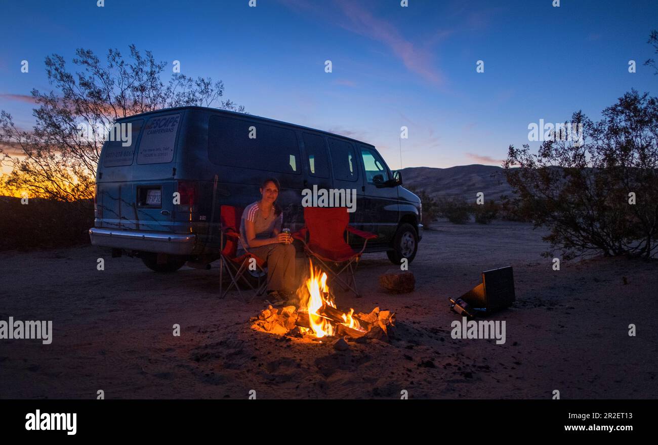 Frau am Lagerfeuer und Minibus auf den Sanddünen von Kelso im Mojave-Nationalpark bei Sonnenuntergang Stockfoto