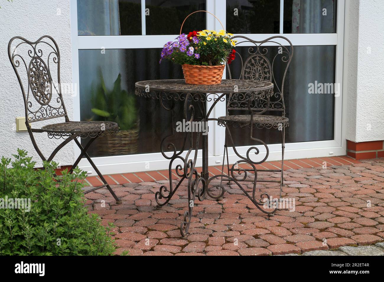 Metalltisch mit Blumenkorb und Stühlen auf einer kleinen Terrasse Stockfoto