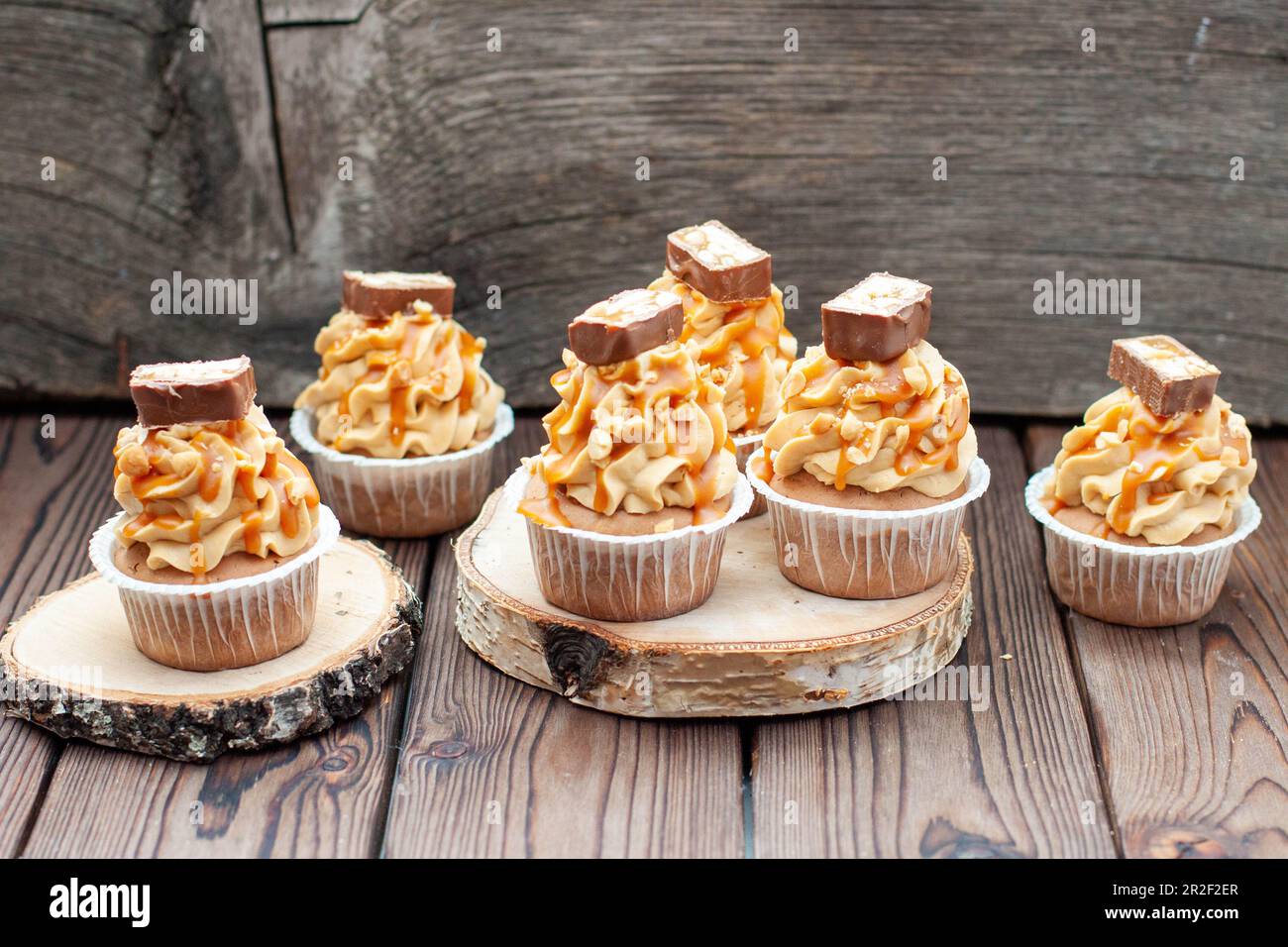 Köstliche Schokoladen-Cupcakes mit Erdnussbutter-Zuckerguss, Schokoladensauce und gesalzener Karamellsauce auf rustikalem Holzhintergrund Stockfoto