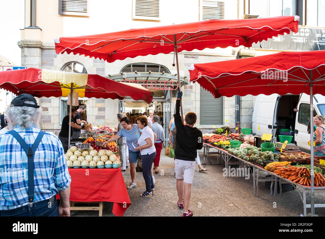 Der junge Mann trägt einen Sonnenschirm durch die Marktstände vor der Markthalle, Les Halles, Redon, Ille-et-Vilaine, Bretagne, Frankreich, Euro Stockfoto