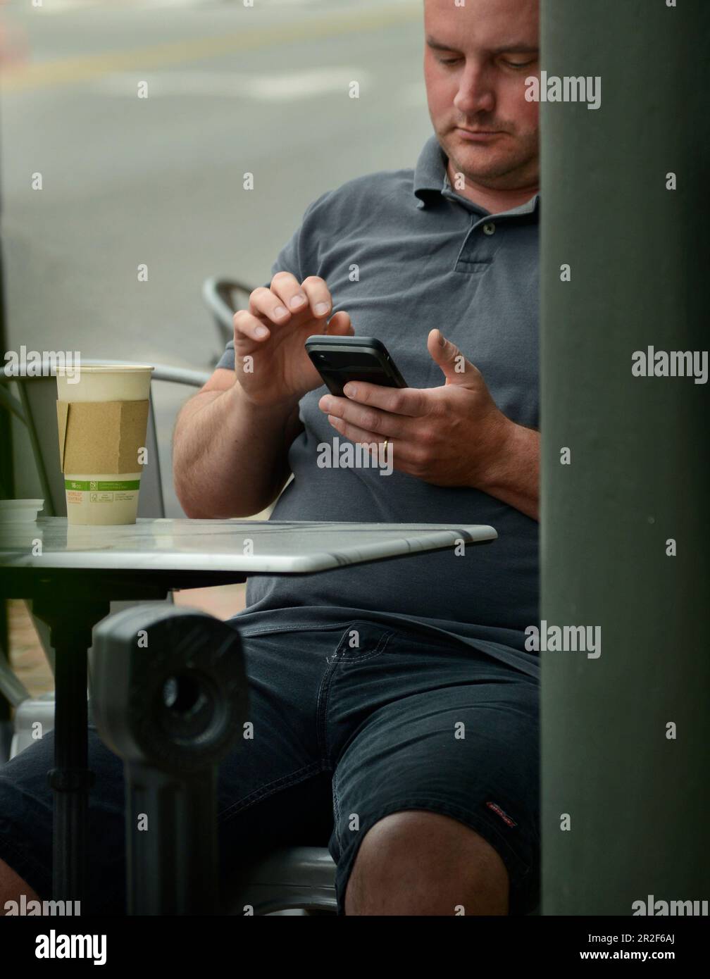 Ein Mann verwendet sein Smartphone, um sich an einem Tisch im Freien in einem Café in Abingdon, Virginia, zu entspannen. Stockfoto