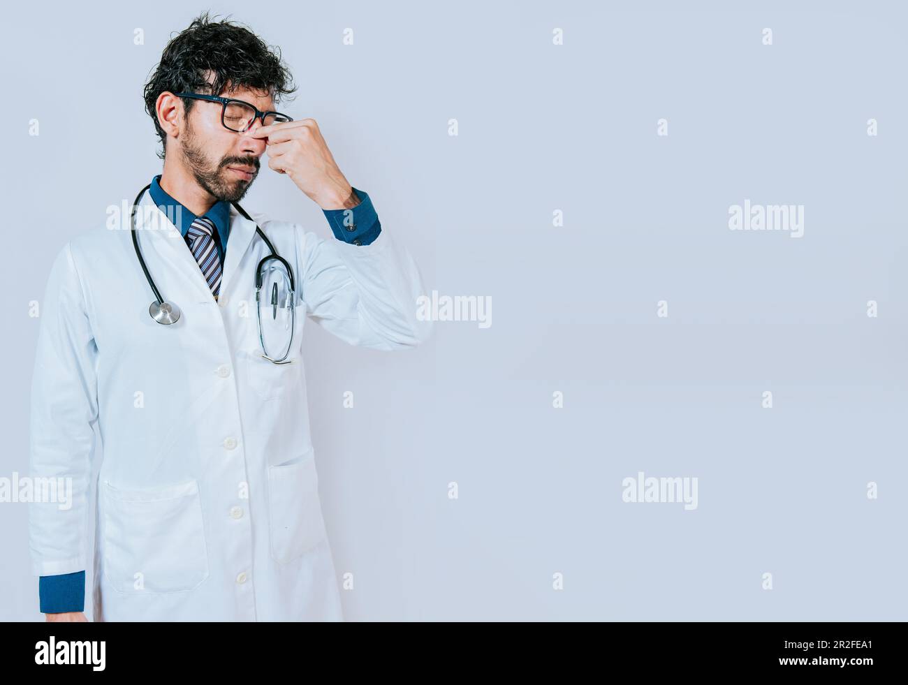 Gestresster und müder Arzt isoliert mit Kopierraum. Müder junger Arzt, der die Nase berührt, isoliert Stockfoto