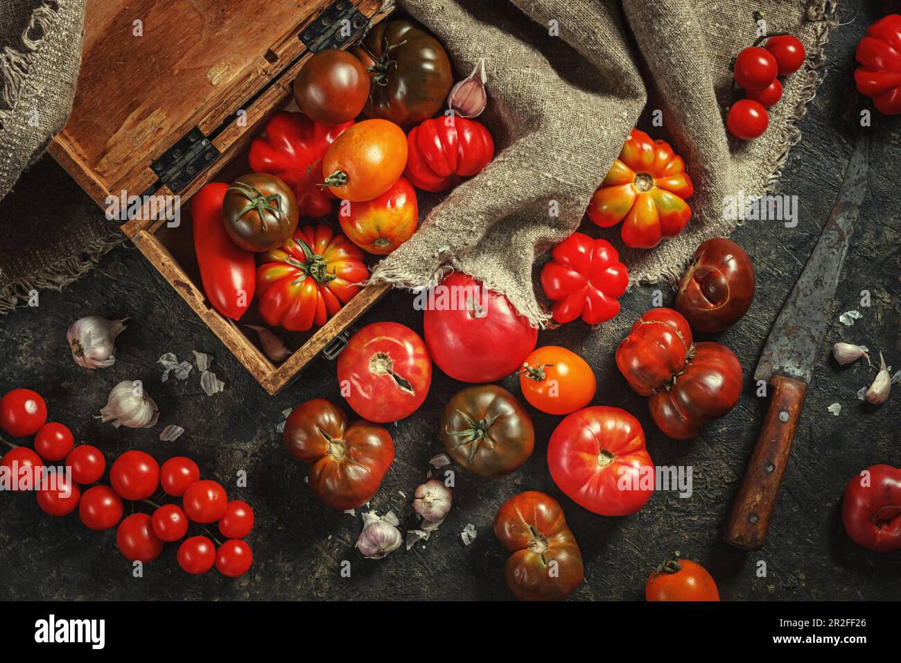 Viele verschiedene Arten, Formen und Größen von Tomaten in einer alten Holzkiste und auf einer dunklen Oberfläche, flach liegend, Draufsicht. Erntekonzept Stockfoto