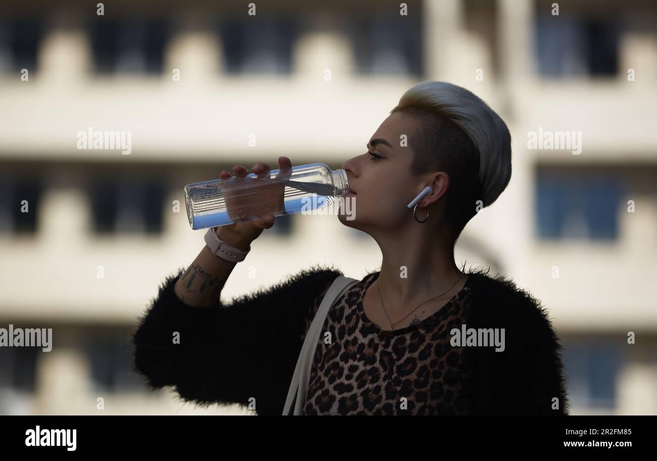 Junge, vielfältige Frau, die Wasser aus einer Glasflasche im Freien trinkt.  Stilvolle Frau mit kurz gefärbtem Haar trinkt Flüssigkeit aus einer wiederverwendbaren  Flasche Stockfotografie - Alamy