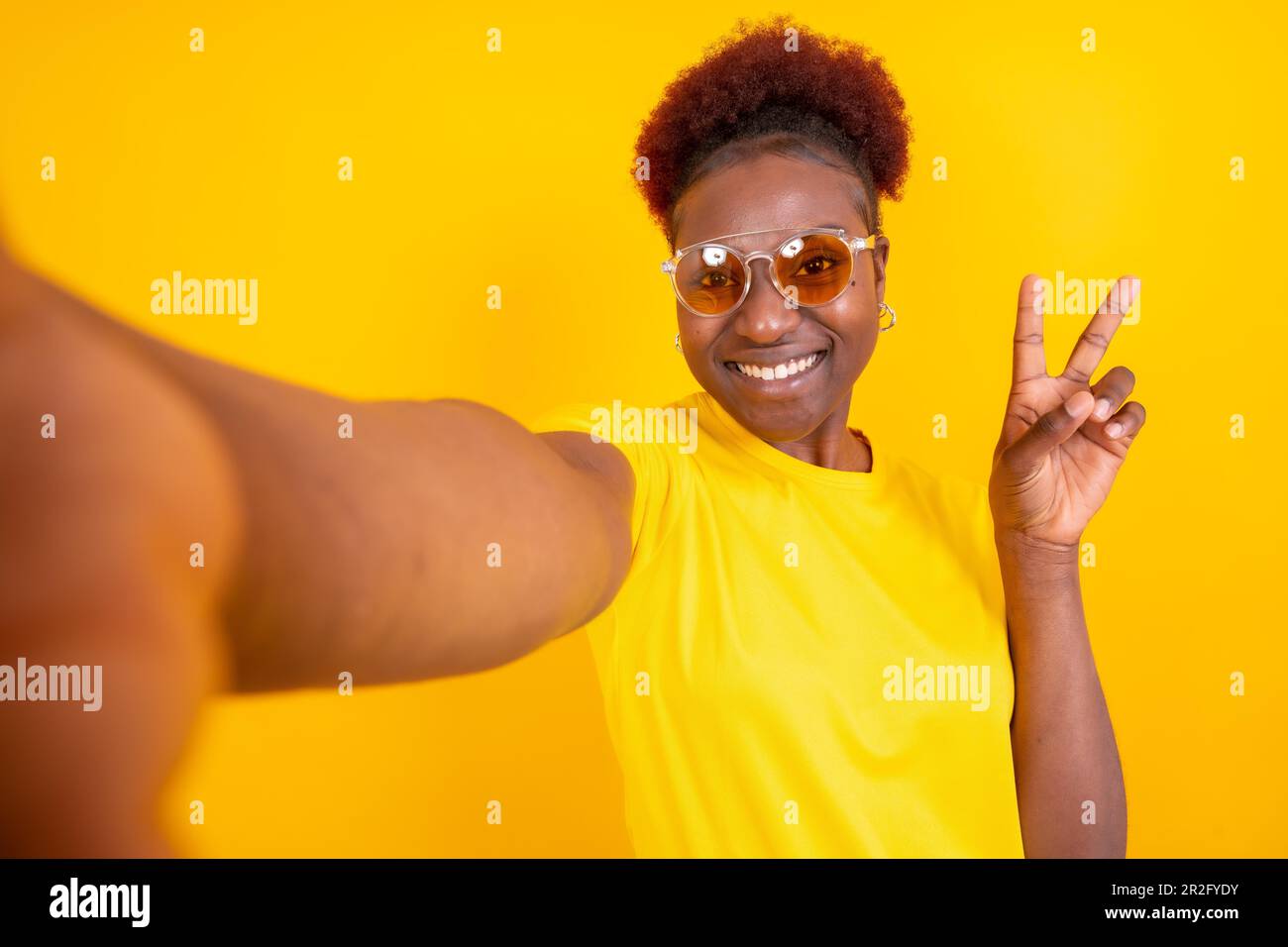 Junge afroamerikanische Frau, isoliert auf gelbem Hintergrund, lächelt und macht ein Selfie, Studioshooting Stockfoto