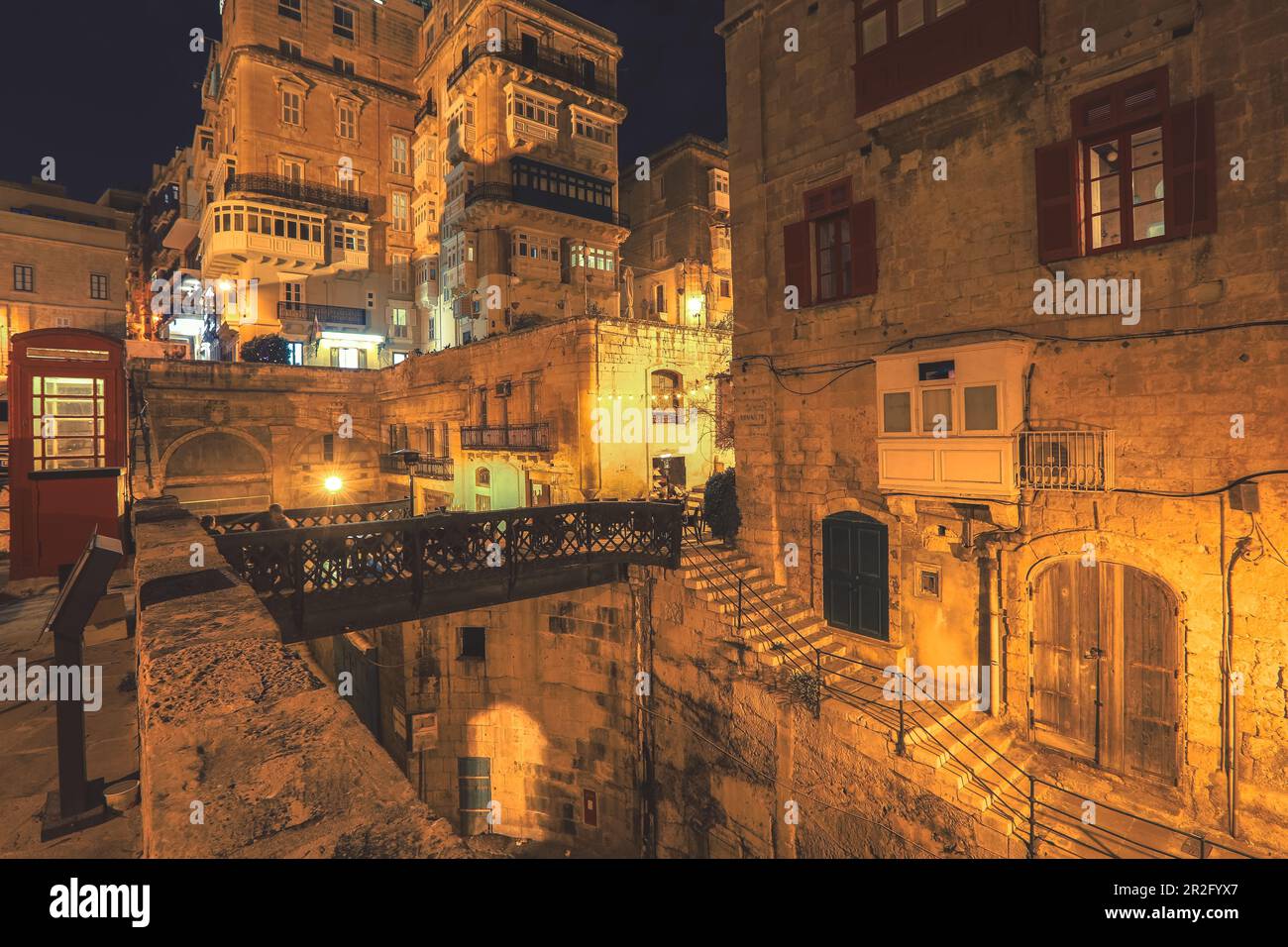 Blick auf die traditionelle maltesische Straße mit roter Telefonzelle bei Nacht, Fensterläden und Balkonen in Valletta, Hauptstadt von Malta Stockfoto