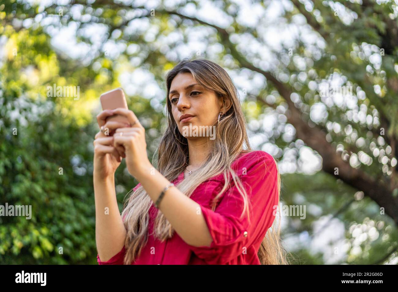 Low-Angle-Betrachtung einer jungen blonden Frau, die ihr Smartphone im Freien benutzt. Modernes Technologiekonzept Stockfoto
