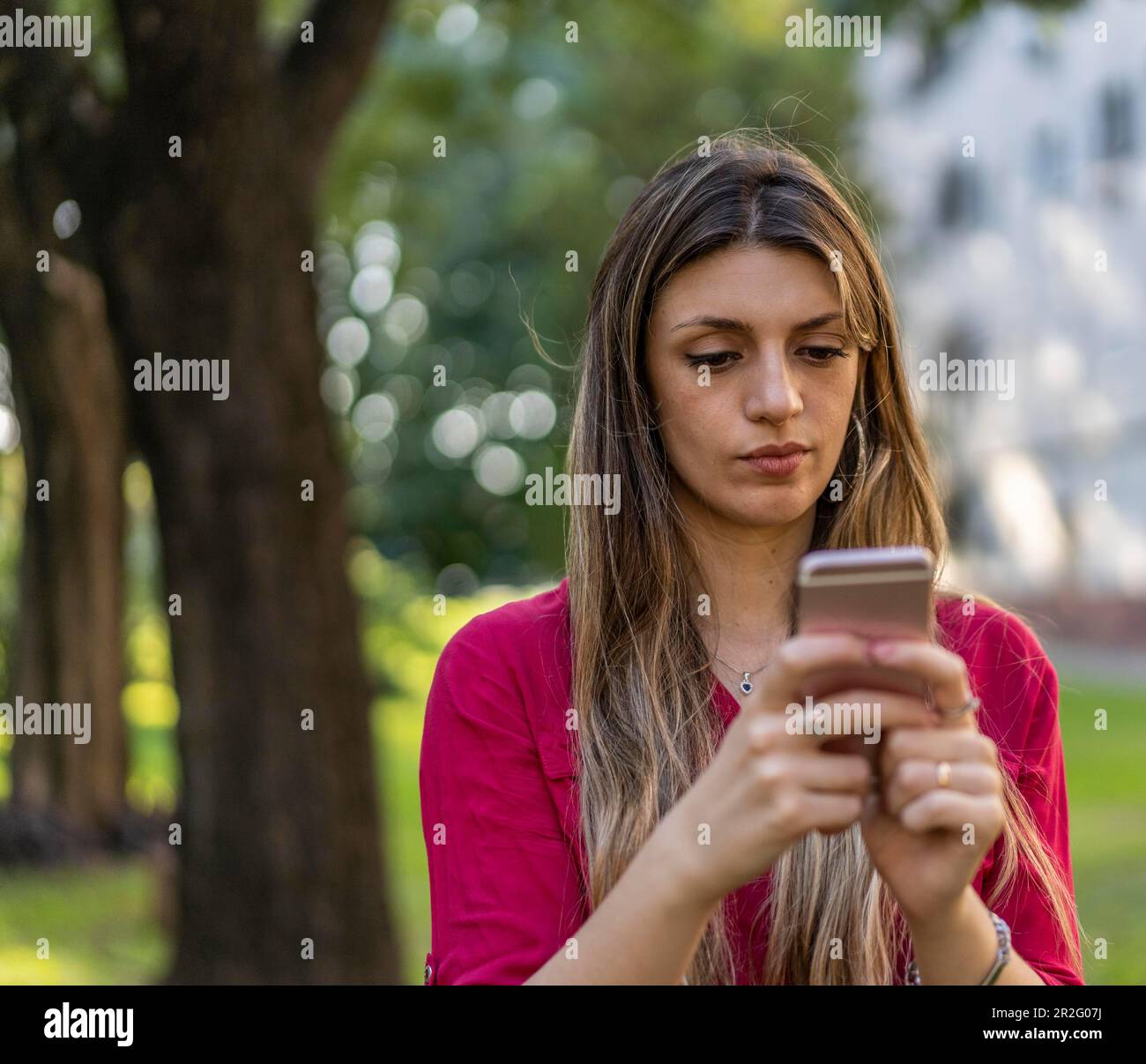 Porträt einer jungen, lächelnden blonden Frau, die draußen unterwegs ist und ein Smartphone benutzt. Modernes Technologiekonzept Stockfoto