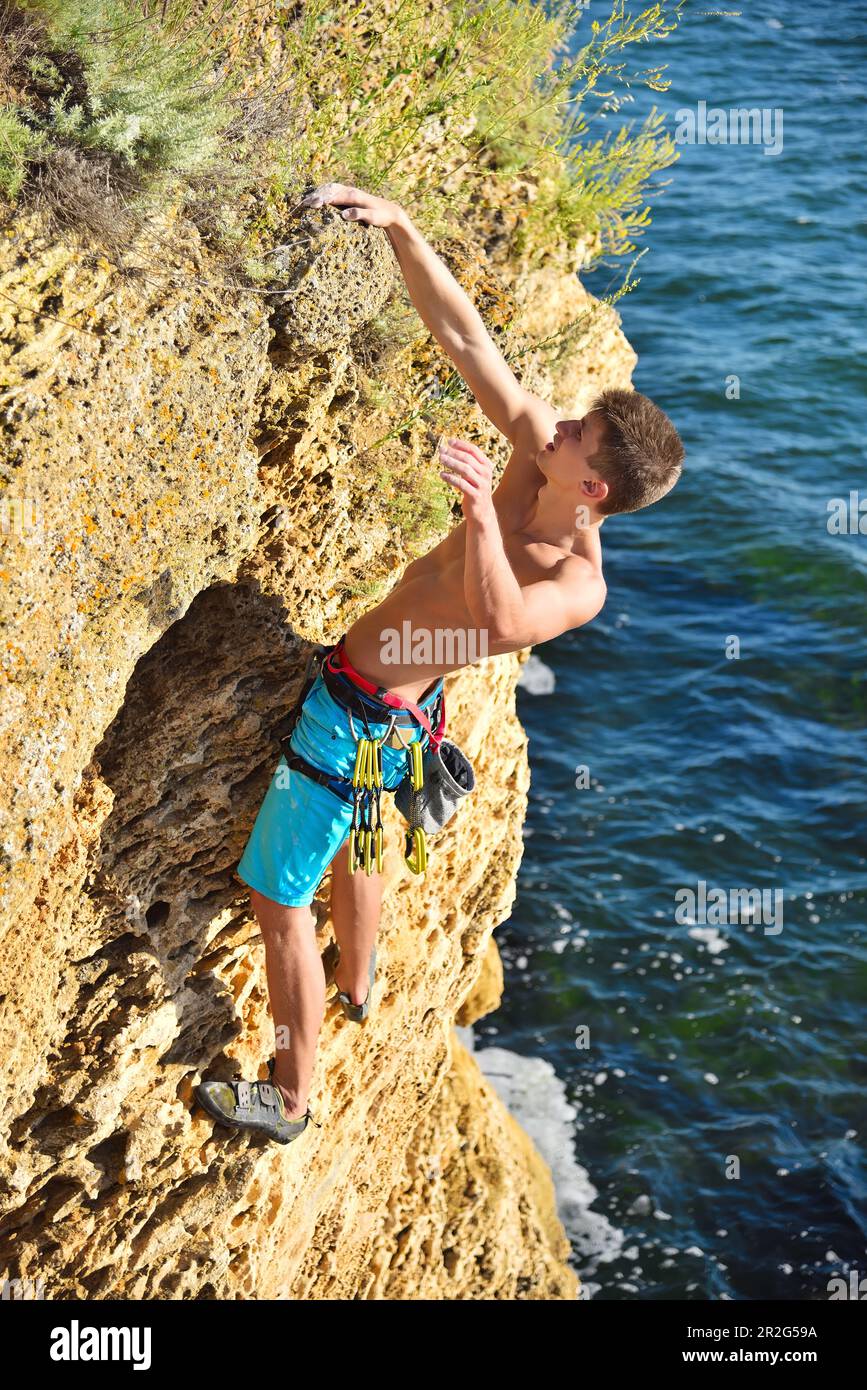 Junger Kletterer, der an einer Klippe auf einem Meereshintergrund hängt Stockfoto