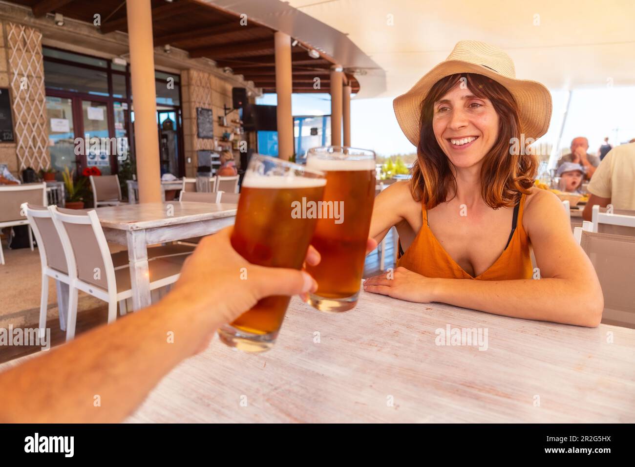 Verabreden Sie sich mit Ihrer Freundin und stoßen Sie mit Bier in einem Restaurant bei Sonnenuntergang am Strand an Stockfoto