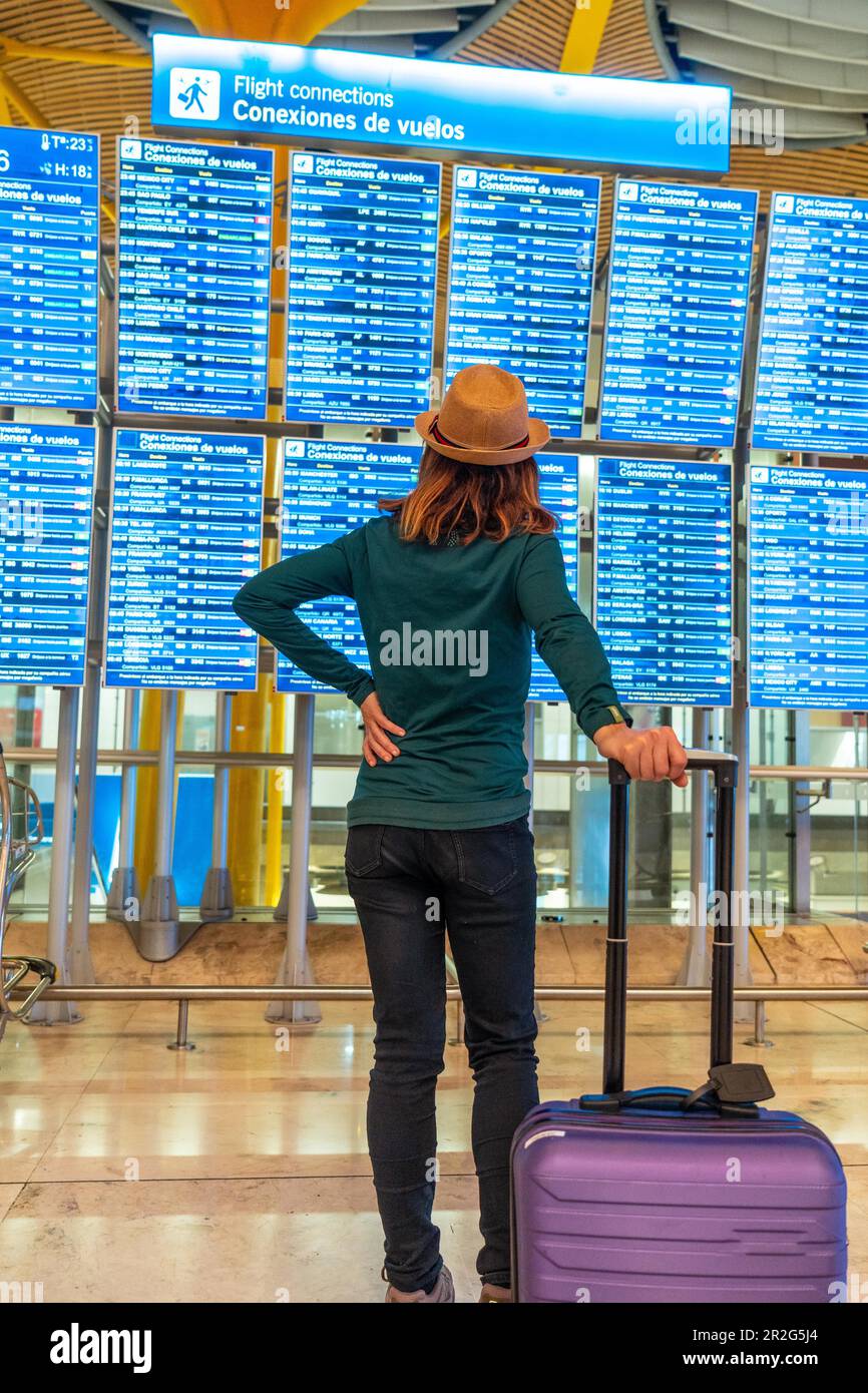 Eine Frau mit Hut und Koffer am Flughafen, die sich die Informationen auf  den Bildschirmen im Terminal ansieht Stockfotografie - Alamy