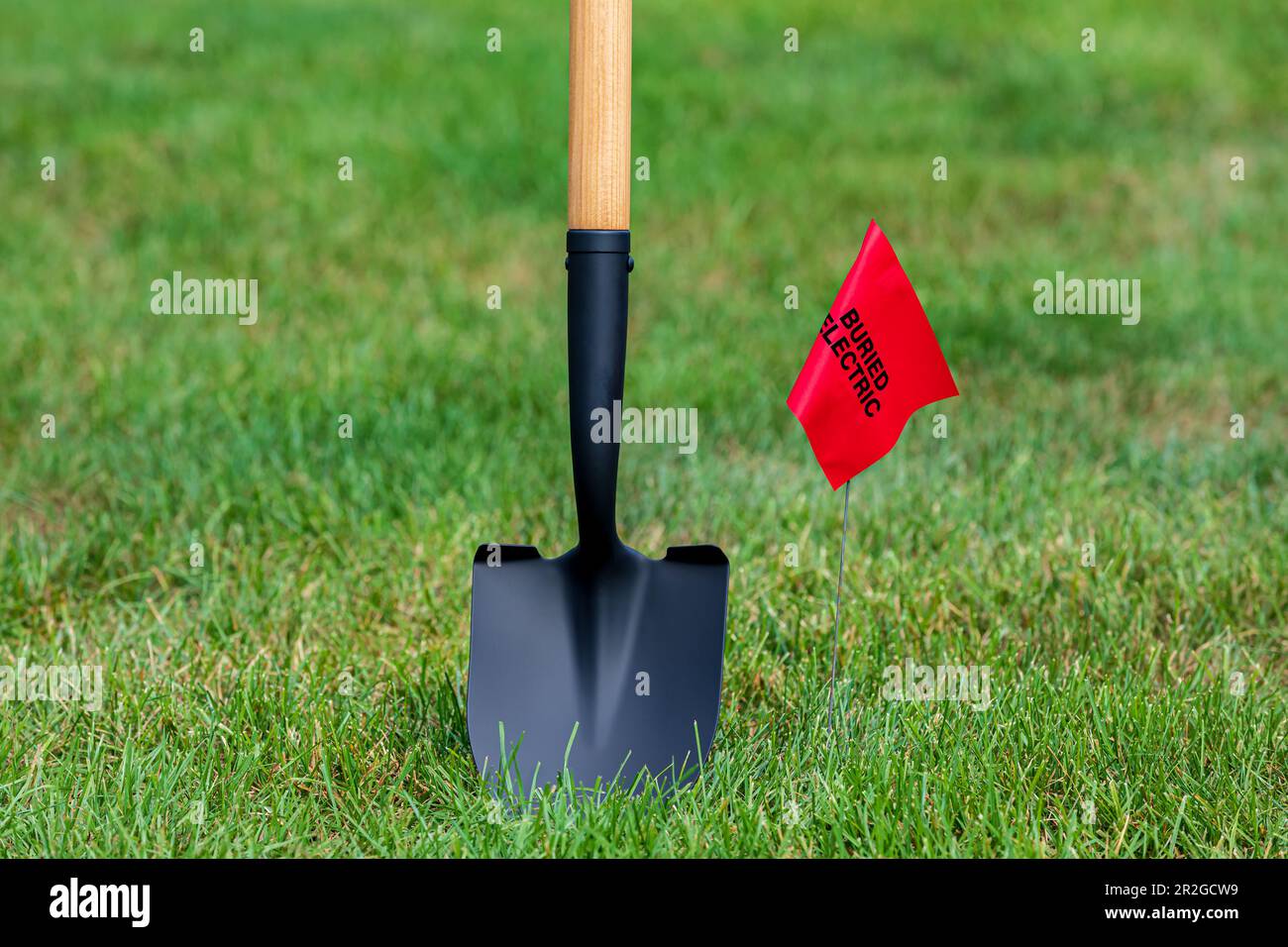 Warnfahne für vergrabene Stromleitungen mit Schaufel. Benachrichtigen Sie das Versorgungsunternehmen, suchen Sie nach einer Firma für unterirdische Versorgungseinrichtungen, rufen Sie an, bevor Sie graben und graben Stockfoto