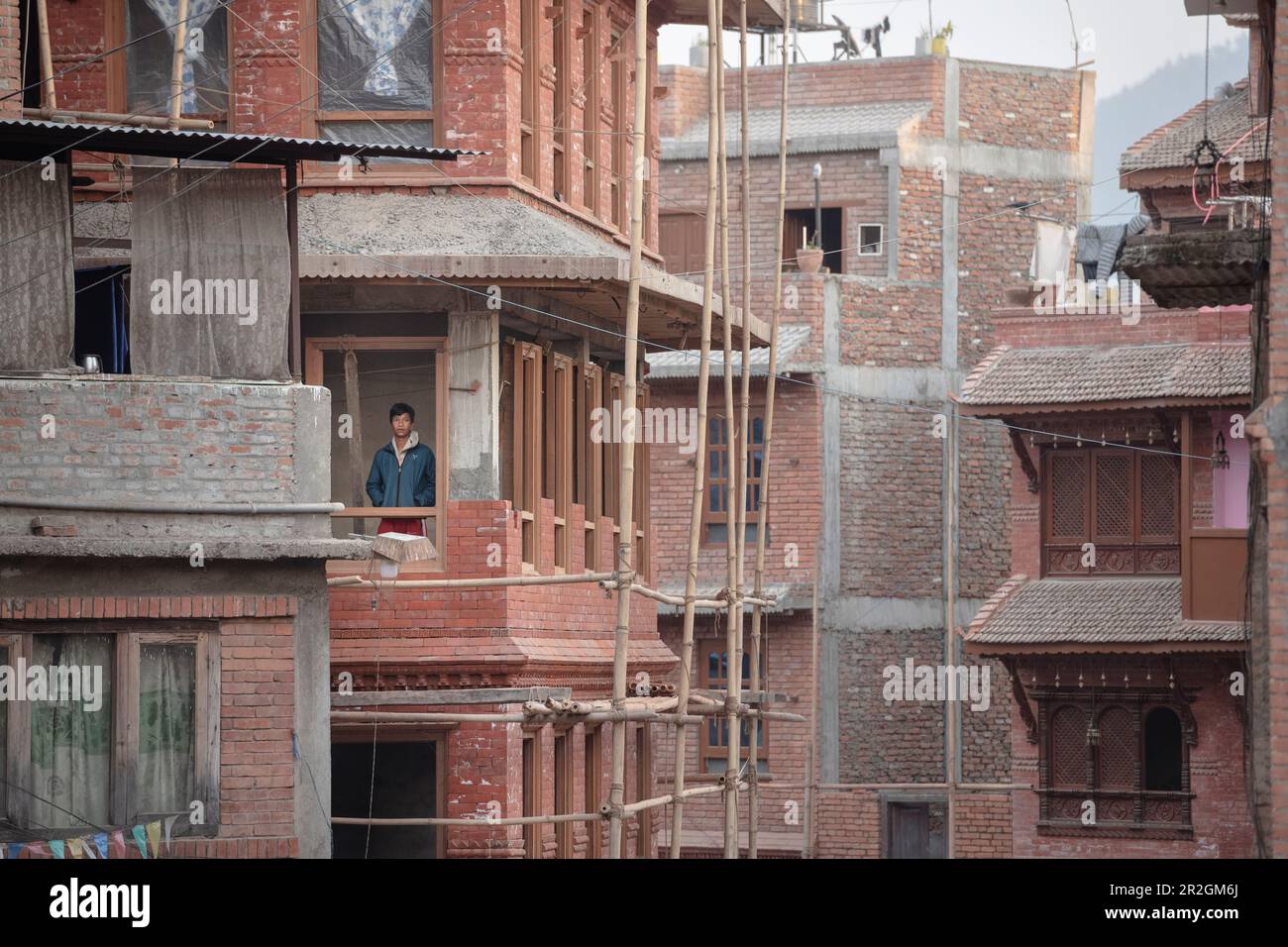 Der Junge schaut aus einem fensterlosen Fenster in einem zerstörten Gebäude in Bhaktapur, Nepal, Himalaya, Asien Stockfoto