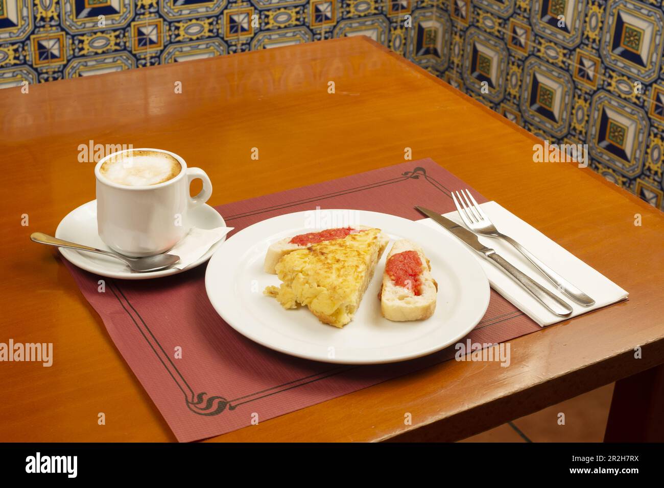 Ein typisches spanisches Frühstück mit Tortilla-Spieß mit Scheiben Pan con Tomate und Kaffee mit Milch in einer Tasse auf einem Holztisch Stockfoto