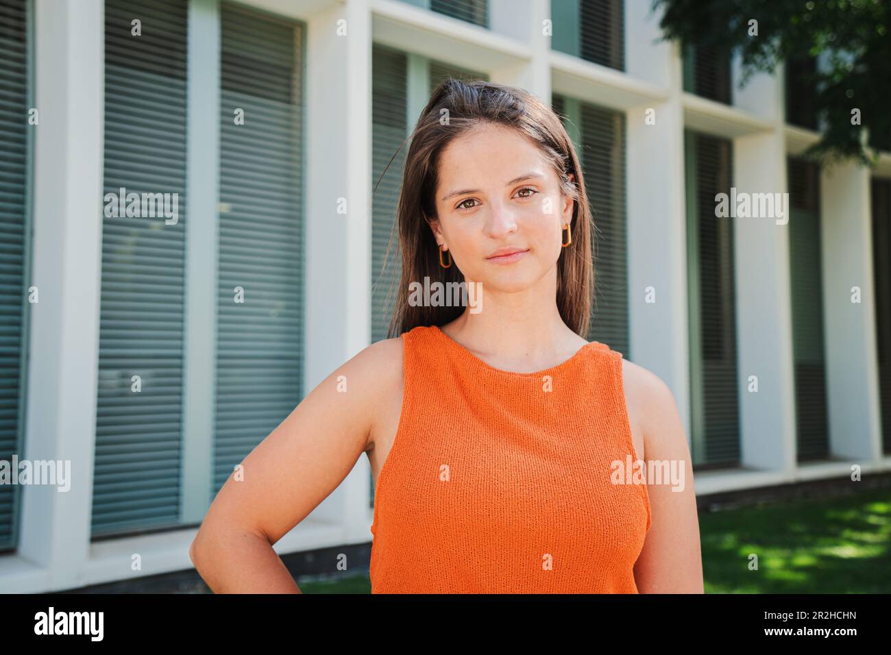 Eine seriöse junge weiße Teenagerin, die in die Kamera schaut, mit entspannten Emotionen und sanftem Gesichtsausdruck draußen. Porträt einer selbstbewussten, ruhigen Frau, die für ein Foto posiert und mit der Hand auf der Hüfte steht. Hochwertiges Foto Stockfoto