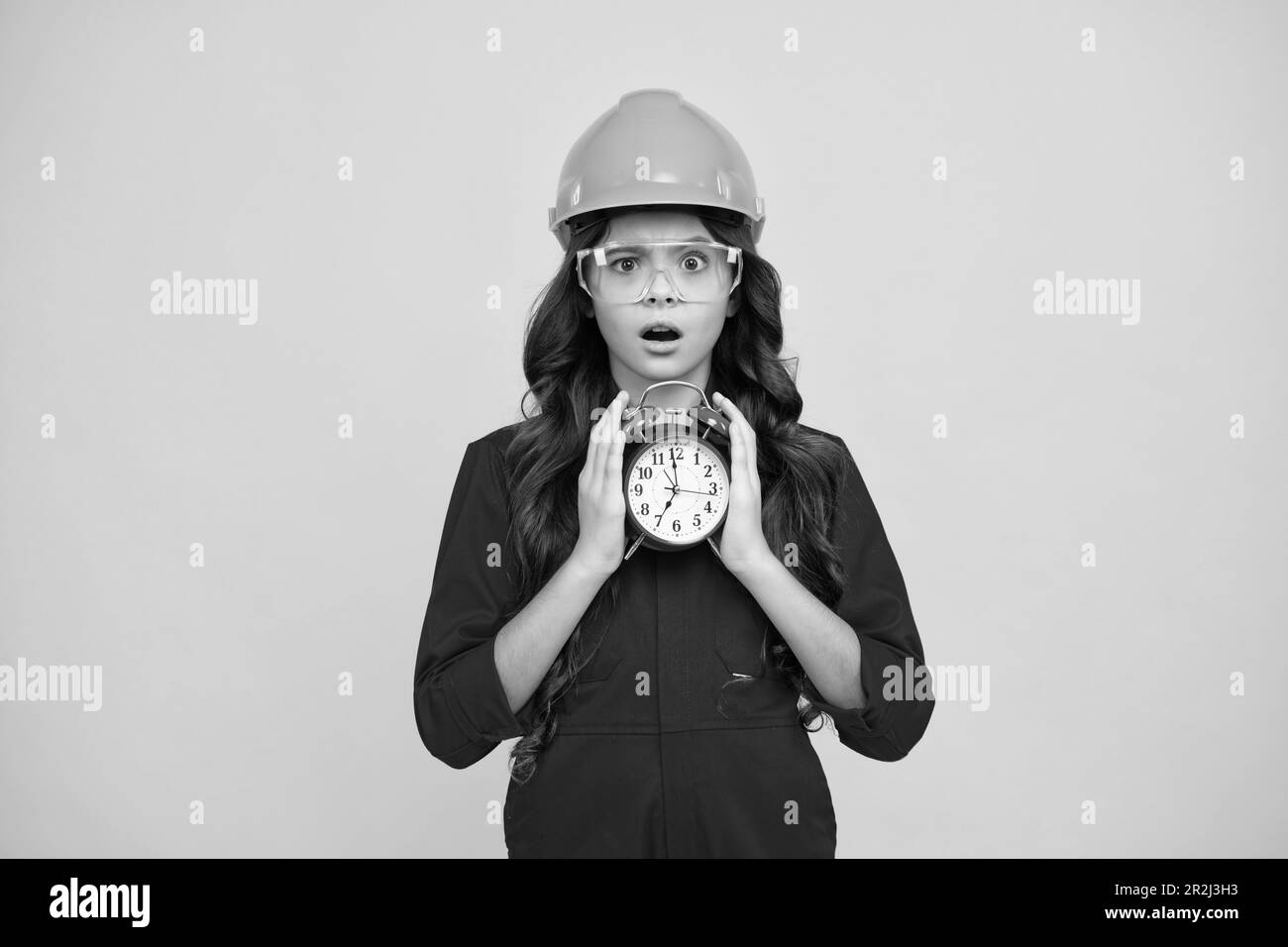 Überrascht Teenager Mädchen. Glücklich lächelnd Teenager Mädchen in Baumeister Helm und Wecker. Zeit bis zur Renovierung und Reparatur. Kind in Hut. Kinderbauer. Stockfoto