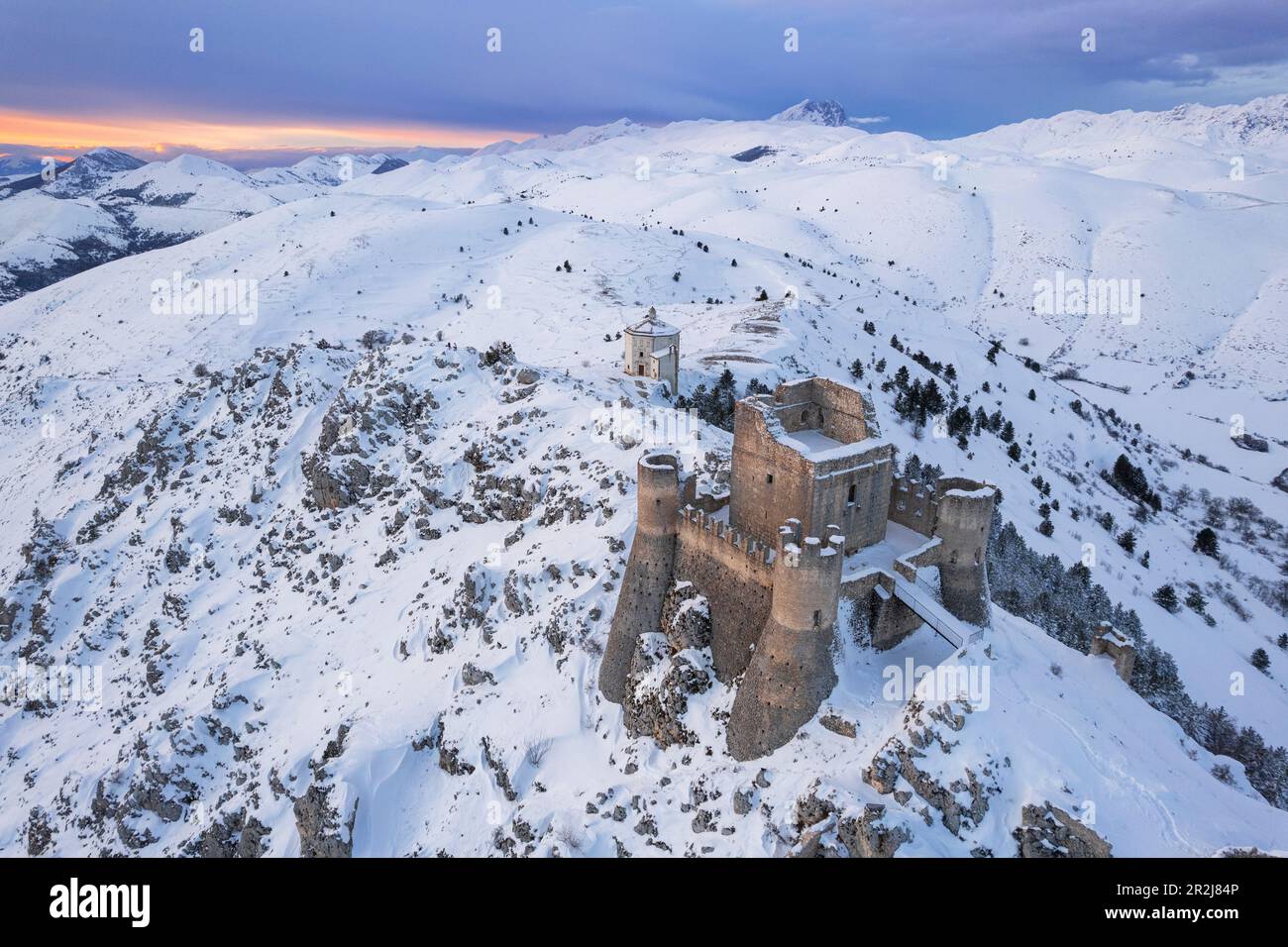 Unvergleichlicher Winterblick auf die Burg Rocca Calascio und die Kirche Santa Maria della Pietà in der schneebedeckten Landschaft in der Dämmerung, Campo Imperatore Stockfoto