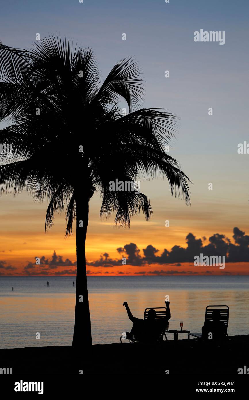 Rentner sitzt auf einem Stuhl bei Sonnenuntergang, tropischer Strand und Paradies Natur, Kaimaninseln, Karibik, Mittelamerika Stockfoto
