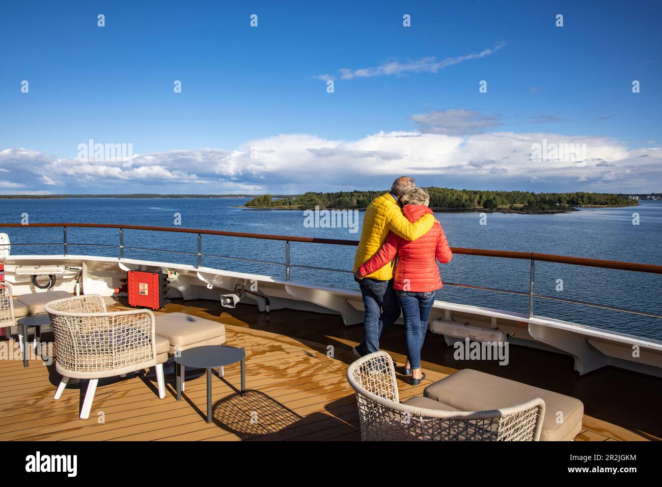 Ein Paar umarmt sich an der Reling auf dem Deck des Expeditionsschiffes World Voyager (Nicko Cruises) mit Küste dahinter, Mariehamn, Aland Inseln, Europa Stockfoto
