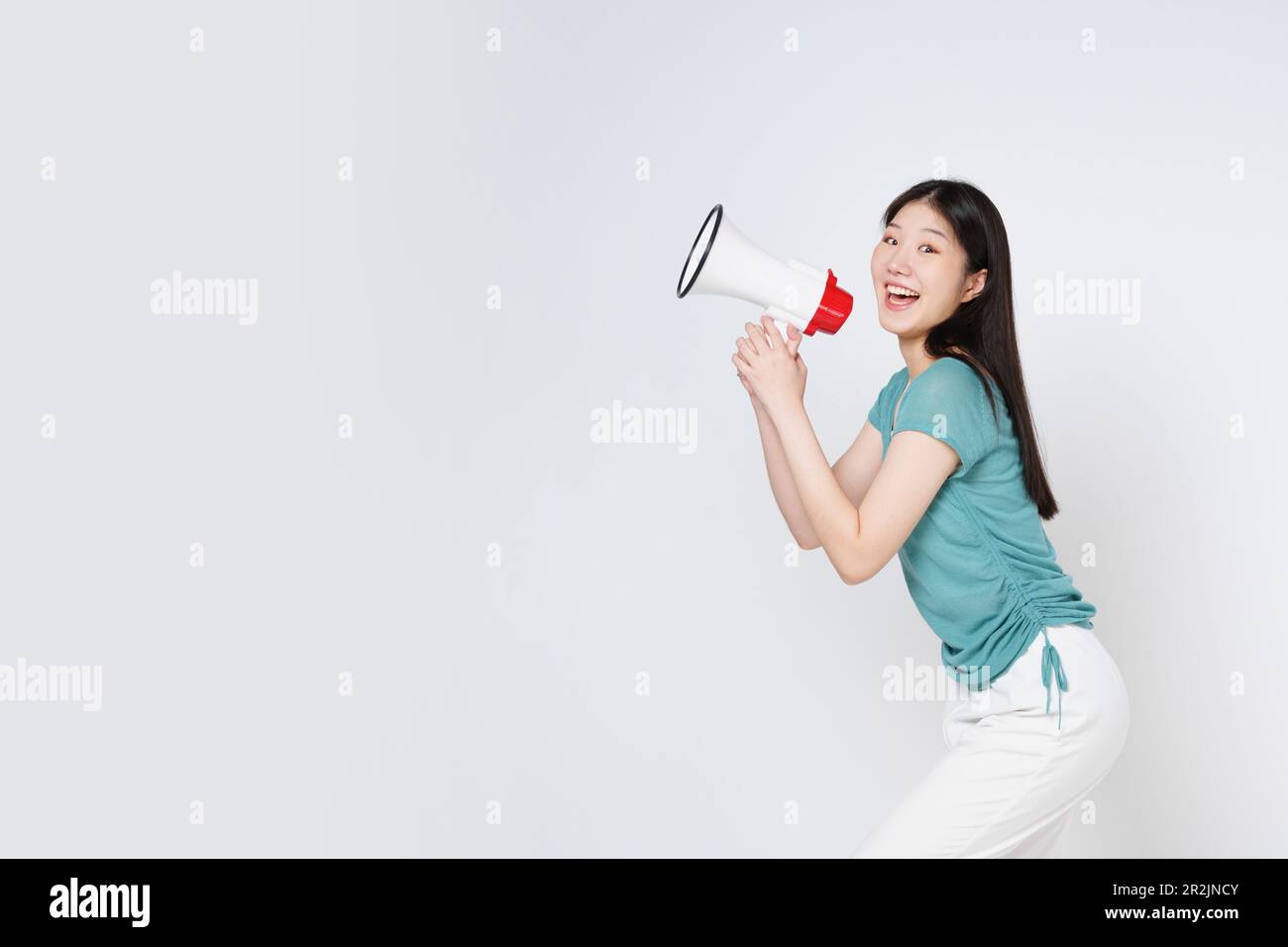 Junge Frau, die Megafon auf weißem Hintergrund isoliert hält. Stockfoto