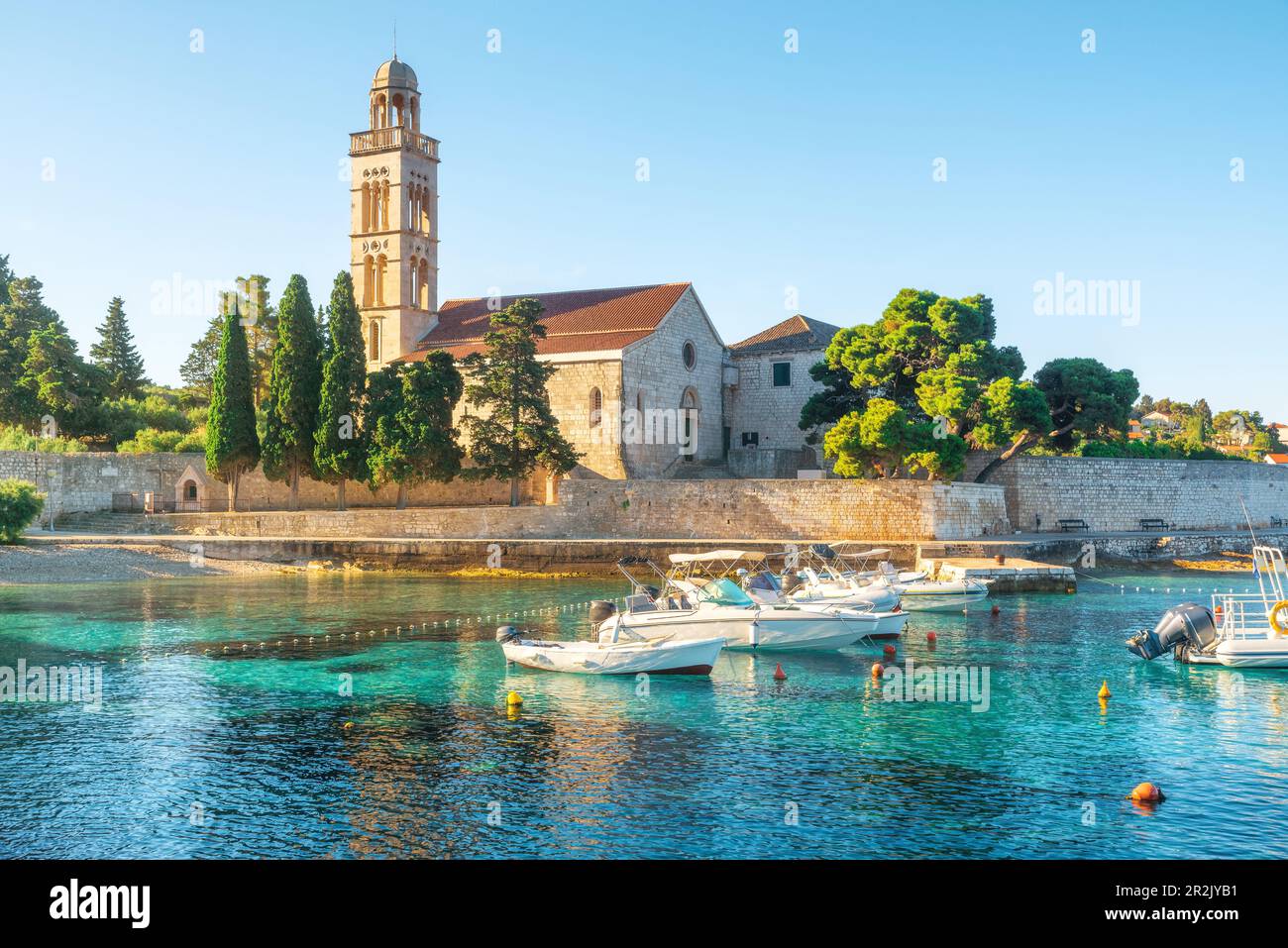 Türkisfarbenes Wasser der Adriatischen Bucht auf der Insel Hvar mit franziskerkloster und Booten in der Region Dalmatien, Kroatien bei Sonnenaufgang. Sommerurlaub destin Stockfoto