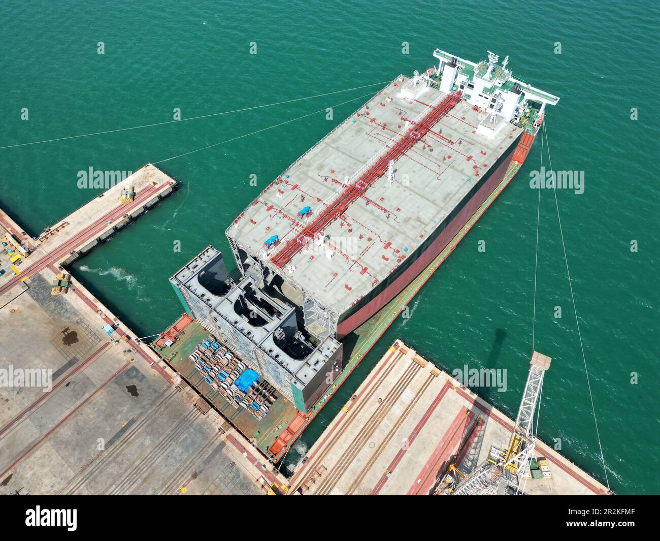 YANTAI, CHINA - 19. MAI 2023 - Ein halb-U-Boot-Schwertransportschiff, das mit Teilen großer Öltanker beladen ist, bereitet sich darauf vor, die Segel eines Schiffes zu setzen Stockfoto