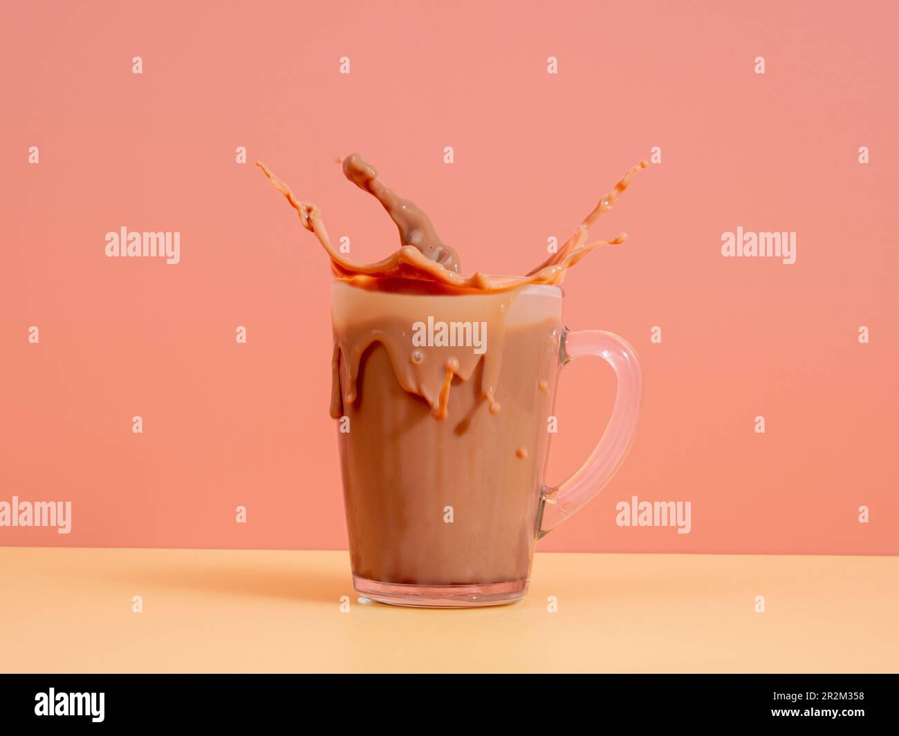 Ein Spritzer Schokoladenmilch aus einem Glas auf pinkfarbenem Hintergrund. Kakao in einem Glas. Ein Spritzer Kakao. Stockfoto