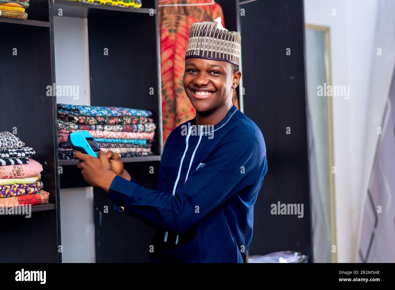 afrikanischer Mann, der auf einem Modemarkt verkauft, mit einem Point-on-Sale-Automaten und lächelnd. Zahlungsart, bargeldlose Transaktion Stockfoto