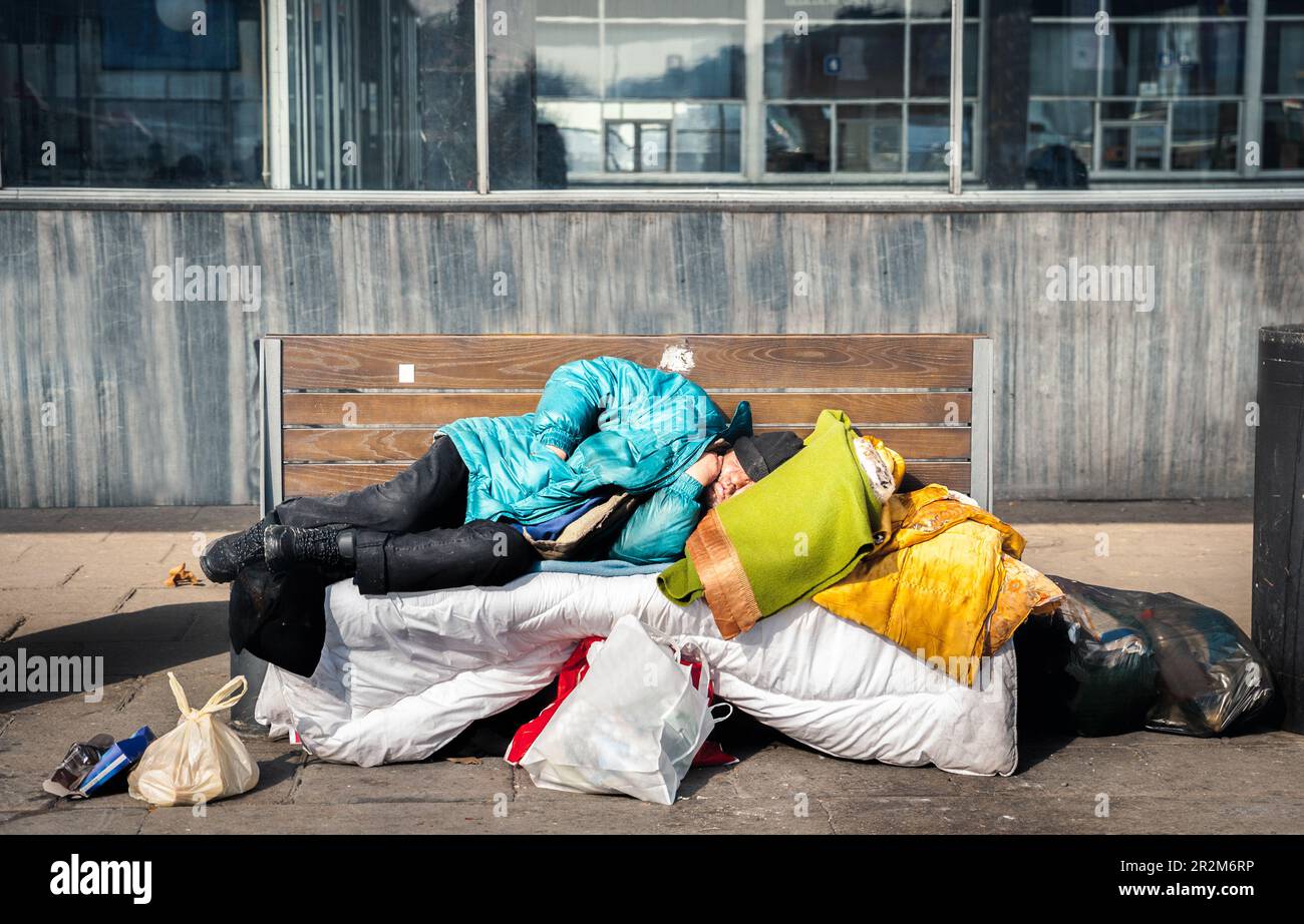 Armer müder, depressiver, hungriger Obdachloser oder Flüchtling, der auf einer Holzbank auf der Stadtstraße schläft, soziales Dokumentarkonzept Stockfoto