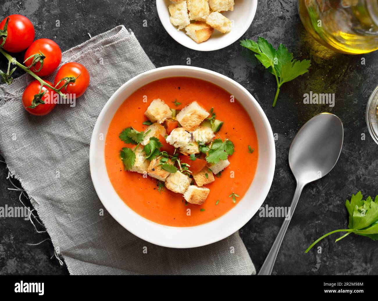 Tomaten-Gazpacho-Suppe mit Croutons in der Schüssel auf dunklem Steinhintergrund. Kalte Sommersuppe. Draufsicht, flach liegend Stockfoto
