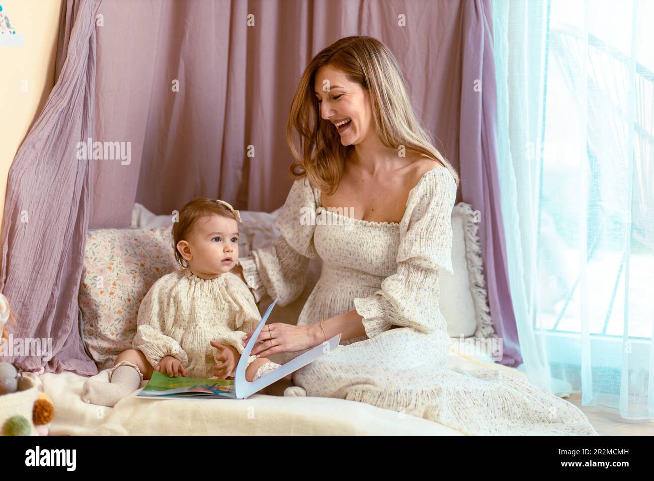 Junge mutter liest mit ihrem einjährigen Mädchen Stockfoto