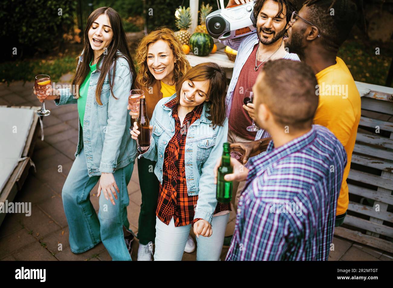 Eine vielfältige Gruppe von Freunden, darunter drei Männer und drei Frauen, von denen eine Afrikanerin ist, genießen alkoholische Getränke (Bier, Cocktails, Wein) und lachen Stockfoto