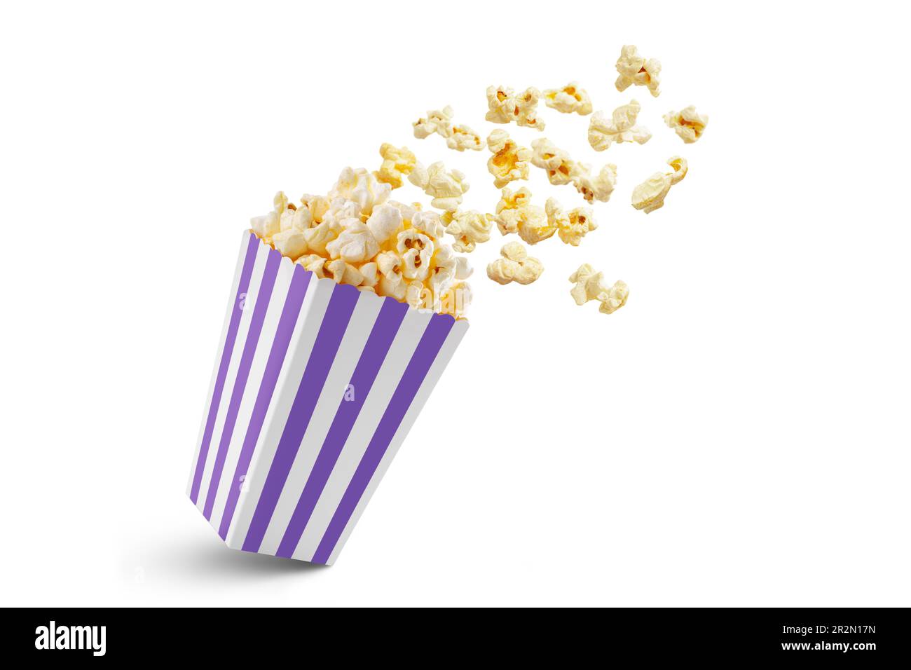 Popcorn fliegt aus einem violett-weiß gestreiften Pappkarton, isoliert auf weißem Hintergrund mit Kopierbereich. Spritzer, Schweben von Popcornkörnern. Stockfoto