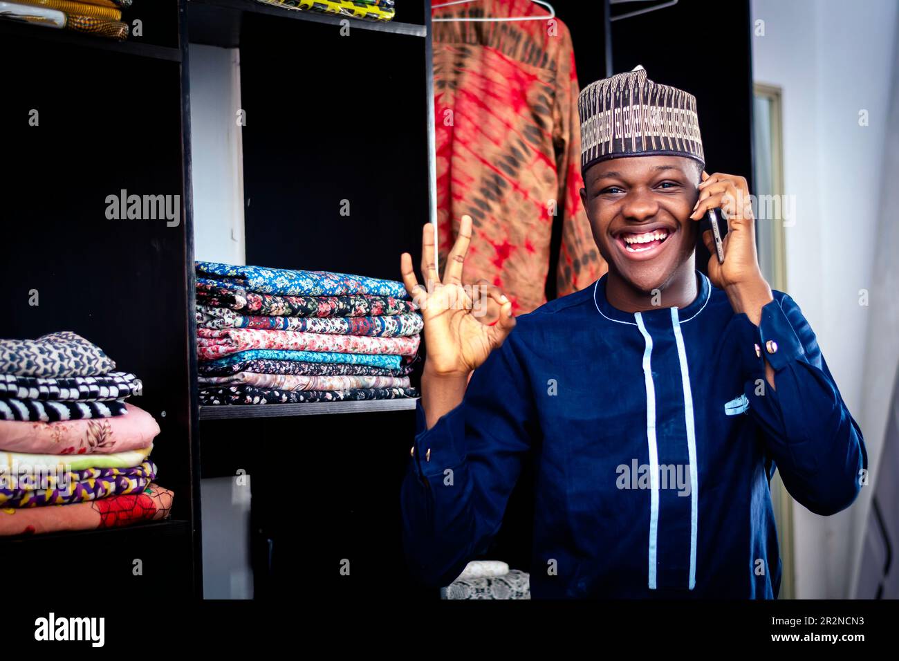 Ein schwarzer Afrikaner, der mit einem Handy in einem afrikanischen Textilladen spricht Stockfoto