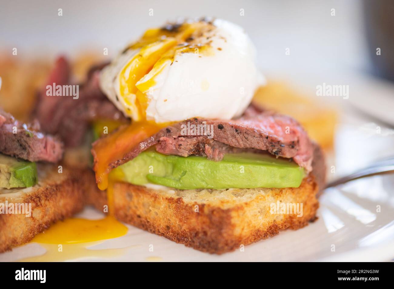Steak benedict Frühstück. Pochierte Eier, gegrilltes Steak und Avocado auf Toast, mit einer Seite Kartoffelrösti. Stockfoto