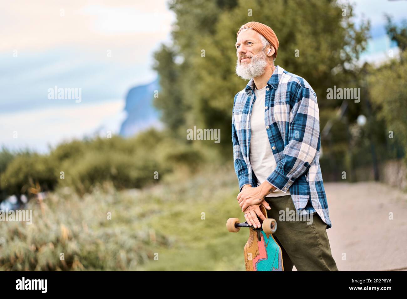 Ein älterer Hipster-Skater steht im Naturpark und hält Schlittschuh. Stockfoto