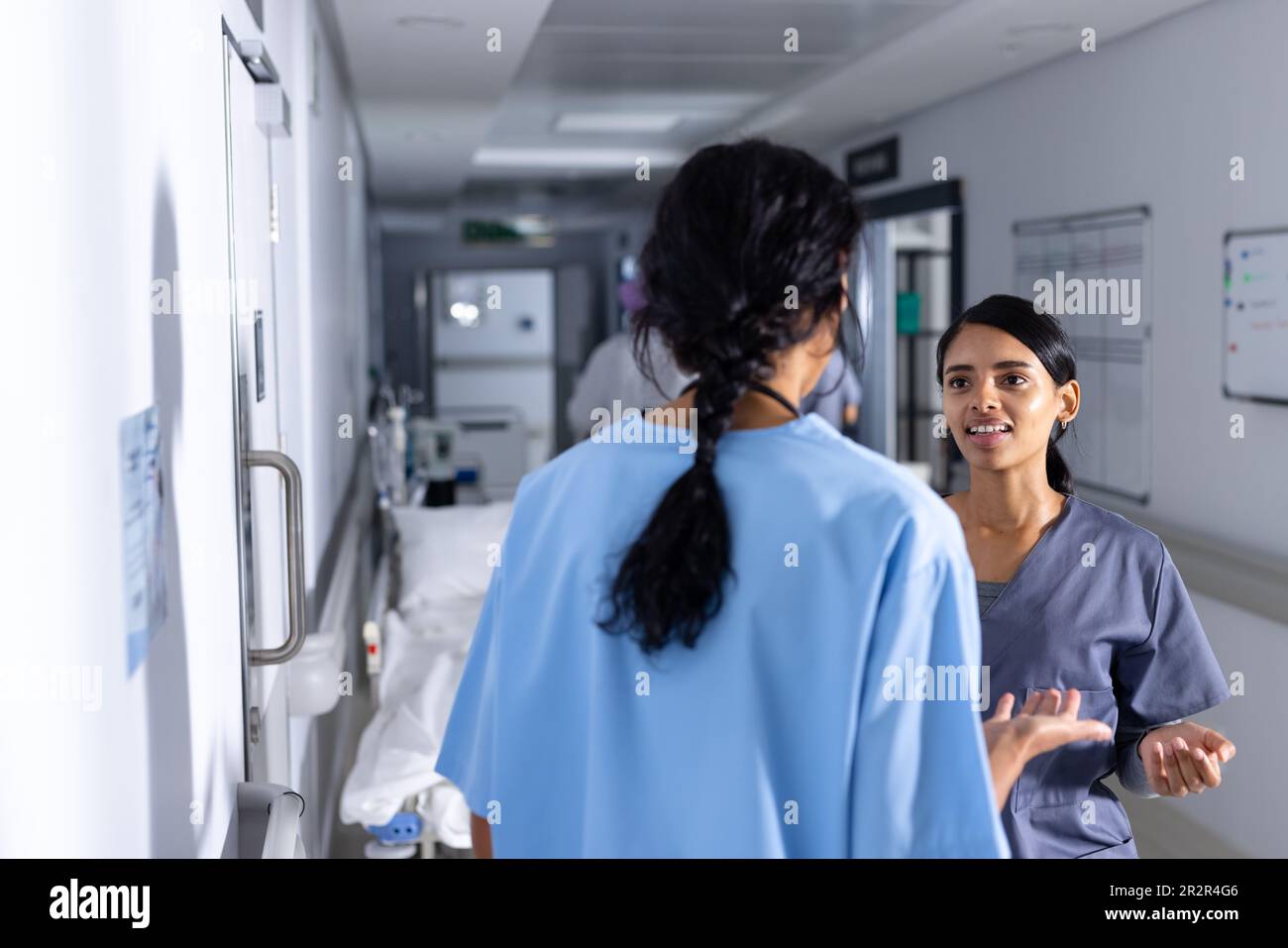 Zwei birassische weibliche Ärzte, die Kittel tragen, sich im Flur im Krankenhaus unterhalten Stockfoto