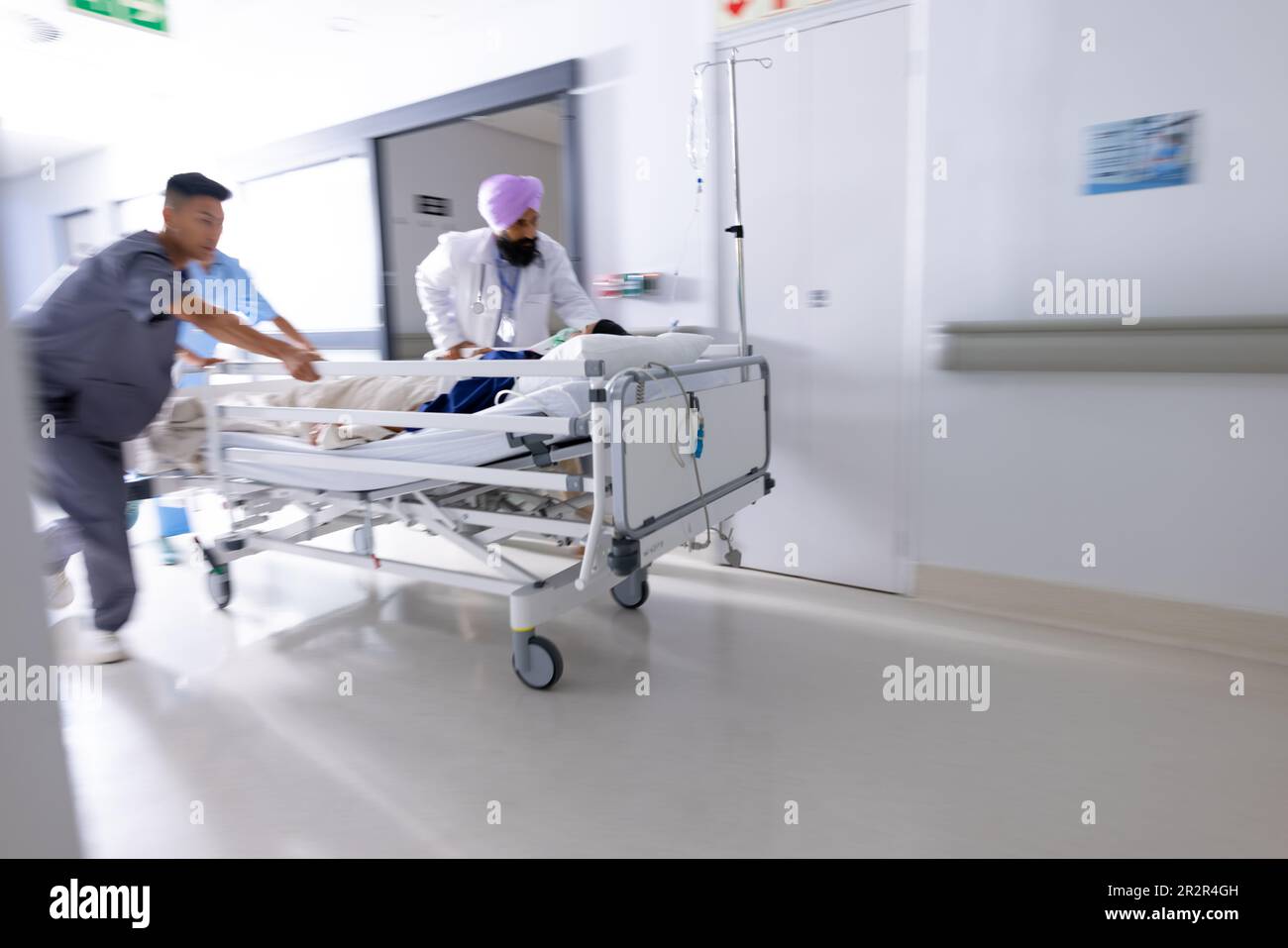 Diverse Ärzte drängen Patienten im Bett im Flur des Krankenhauses Stockfoto